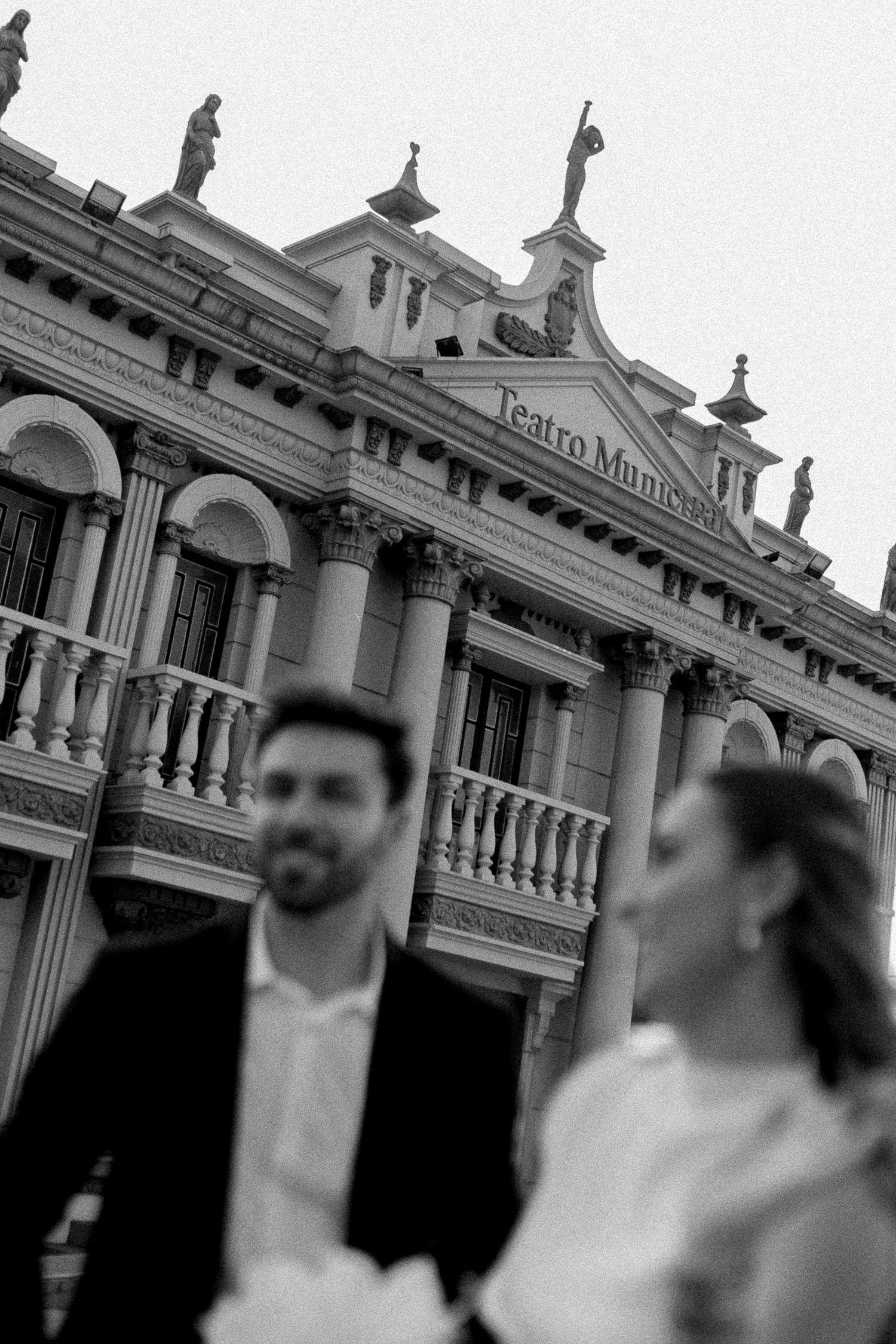 Black and white photo of a couple in formal attire posing before the historic Teatro Municipal building.
