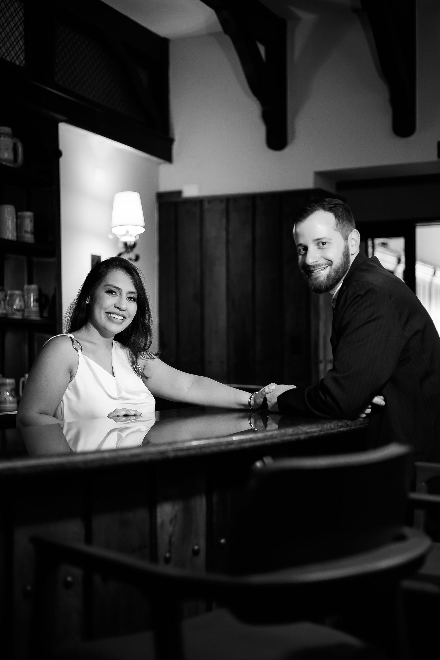 Black and white photo of a smiling couple posing together at a bar counter in an elegant restaurant.