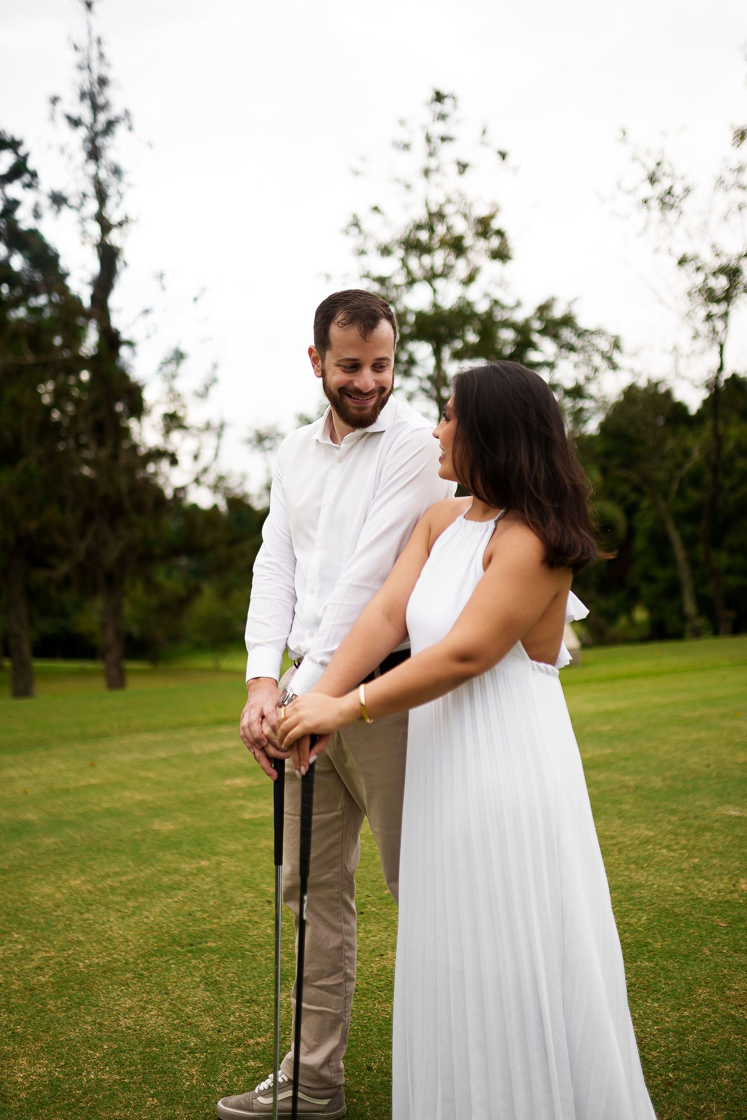Couple in white attire sharing a romantic moment on a golf course, man holding a golf club outdoors.