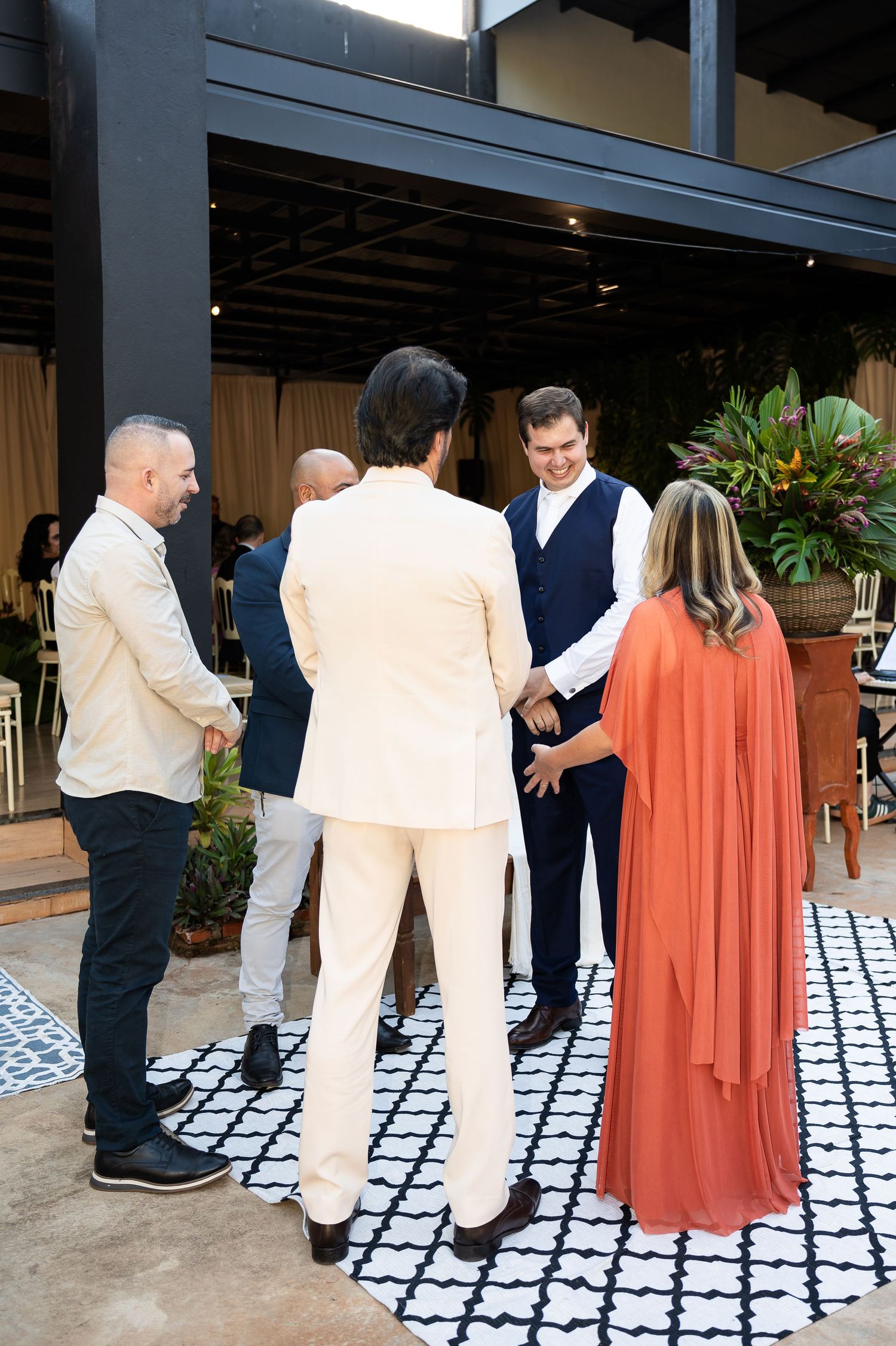 Elegantly dressed guests socializing at an upscale indoor event on a patterned rug.