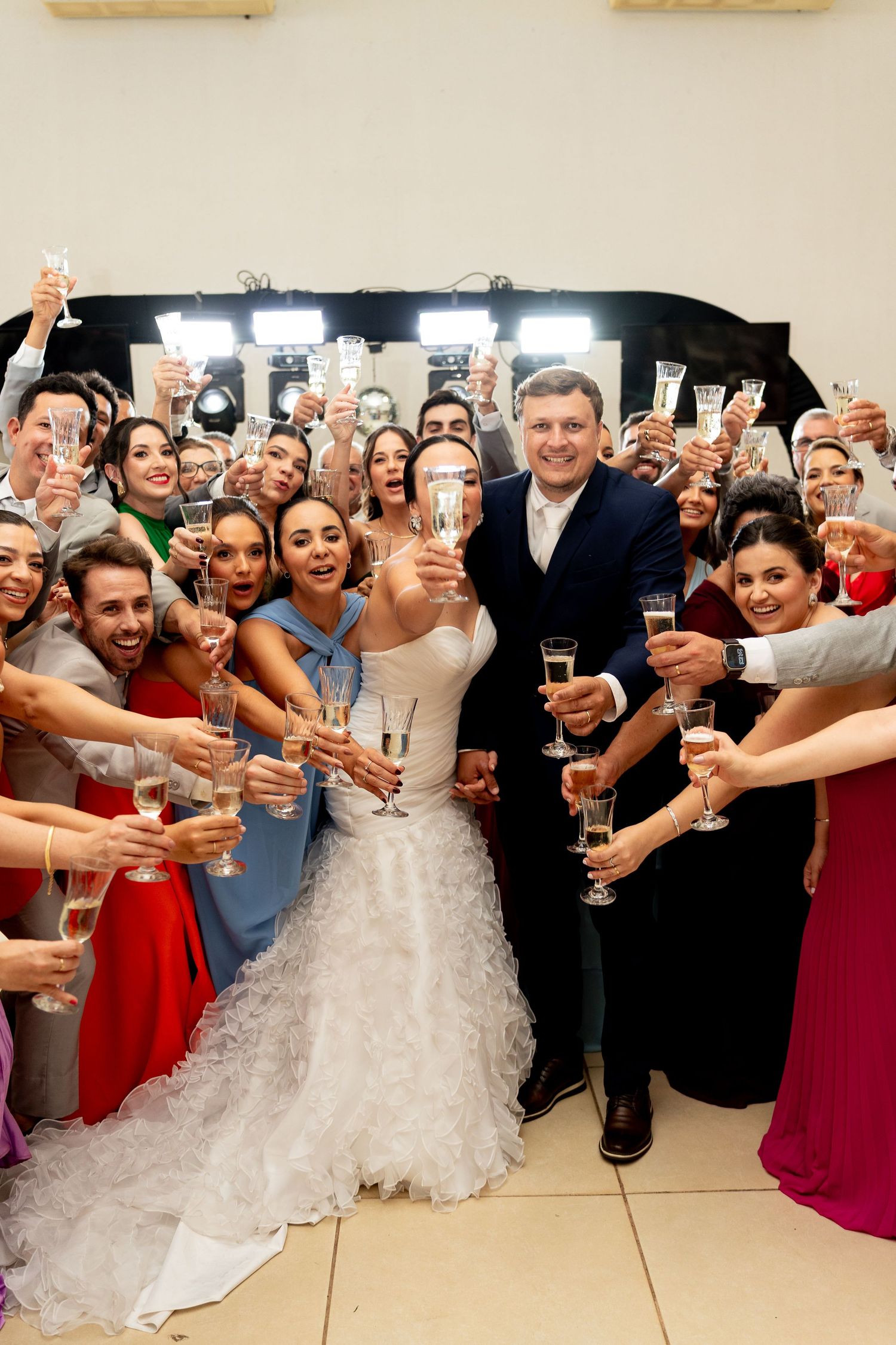 Bride and groom toast champagne with large group of wedding guests at elegant indoor reception celebration.