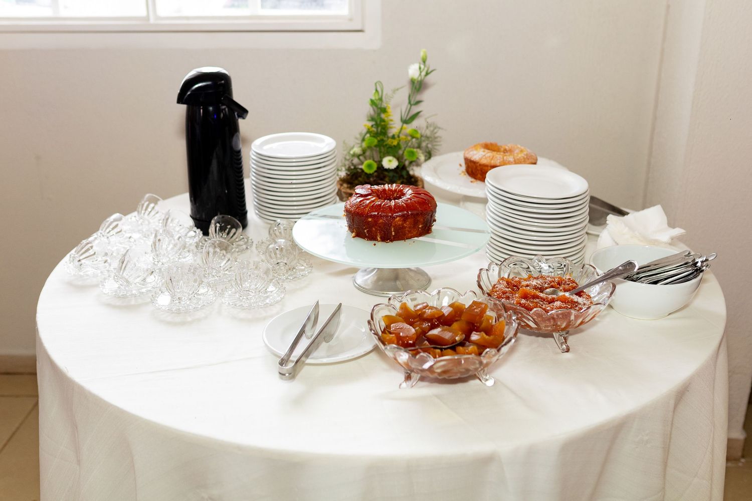 Elegant buffet table with white tablecloth, stacked plates, glassware, cake, and crystal bowls of food.