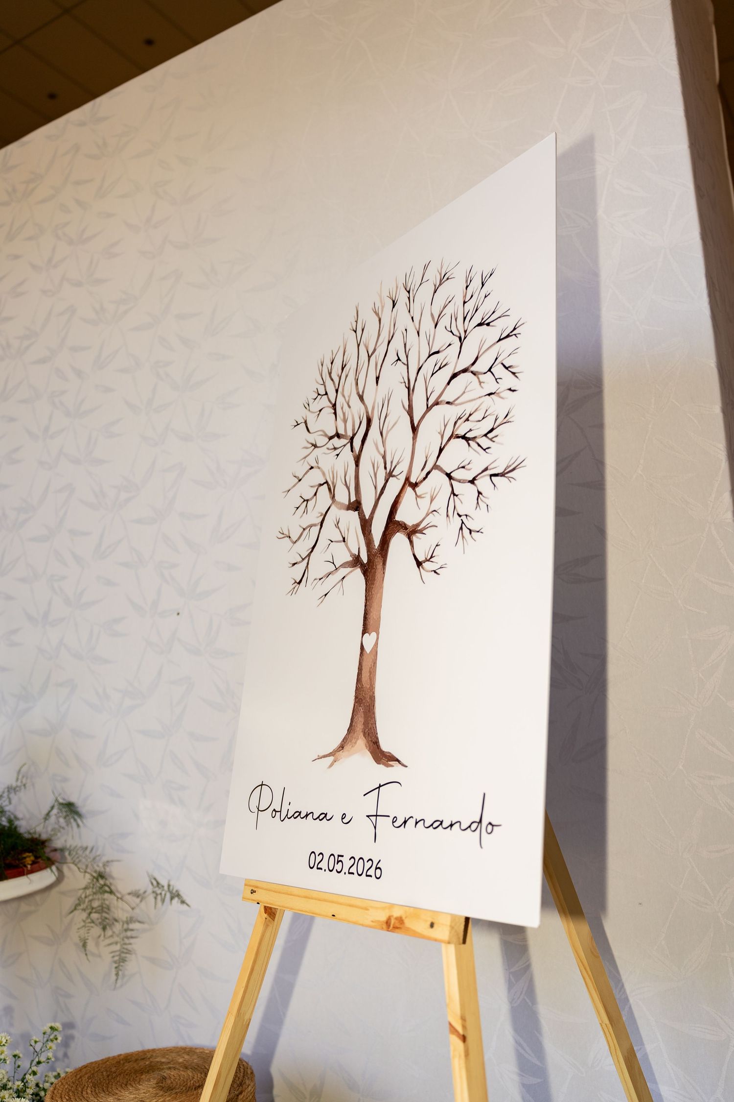 Wedding fingerprint tree canvas on easel displaying Poliana e Fernando 02.05.2026 for guest signatures.