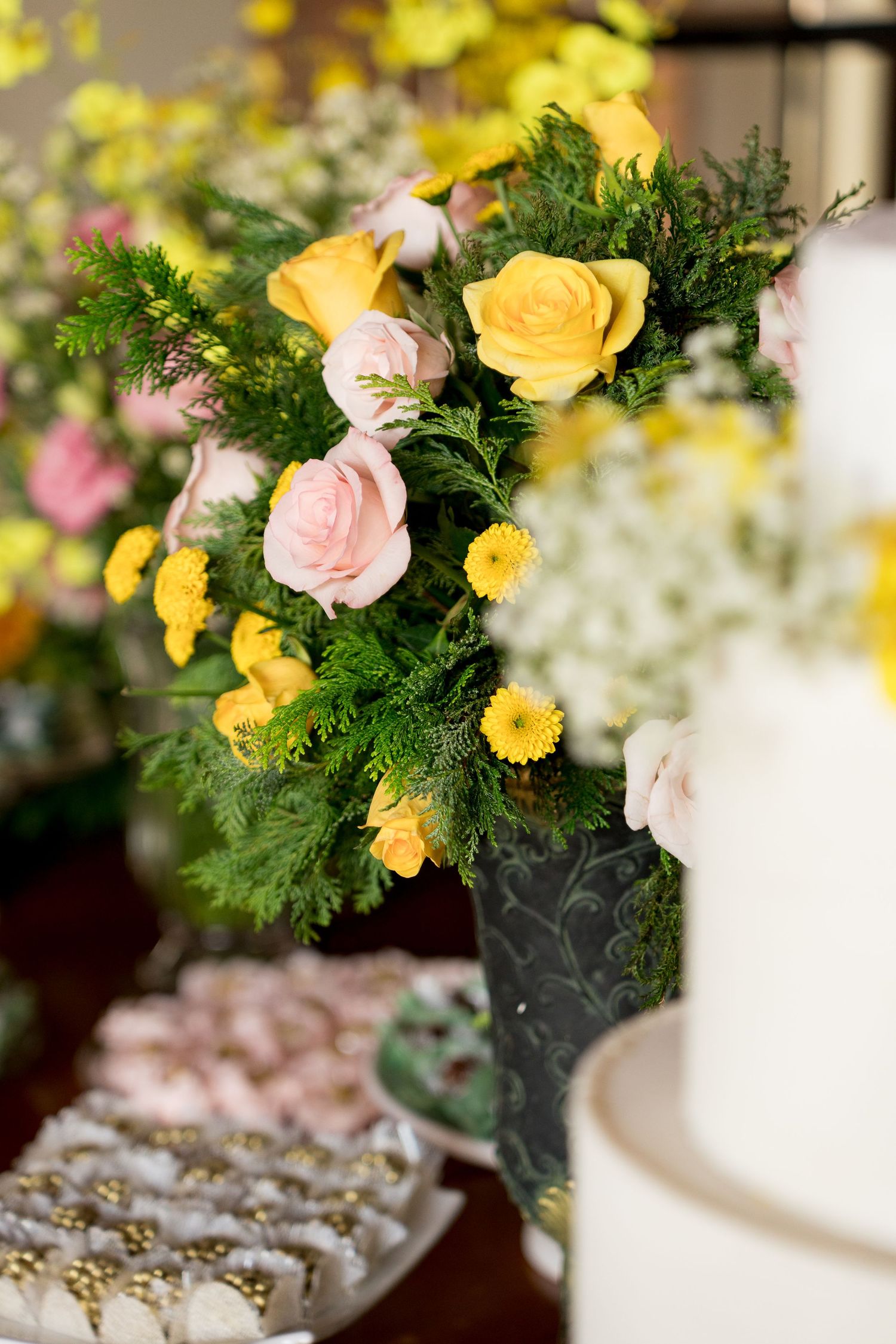 Elegant wedding dessert table with yellow and pink roses arrangement beside a white tiered cake.
