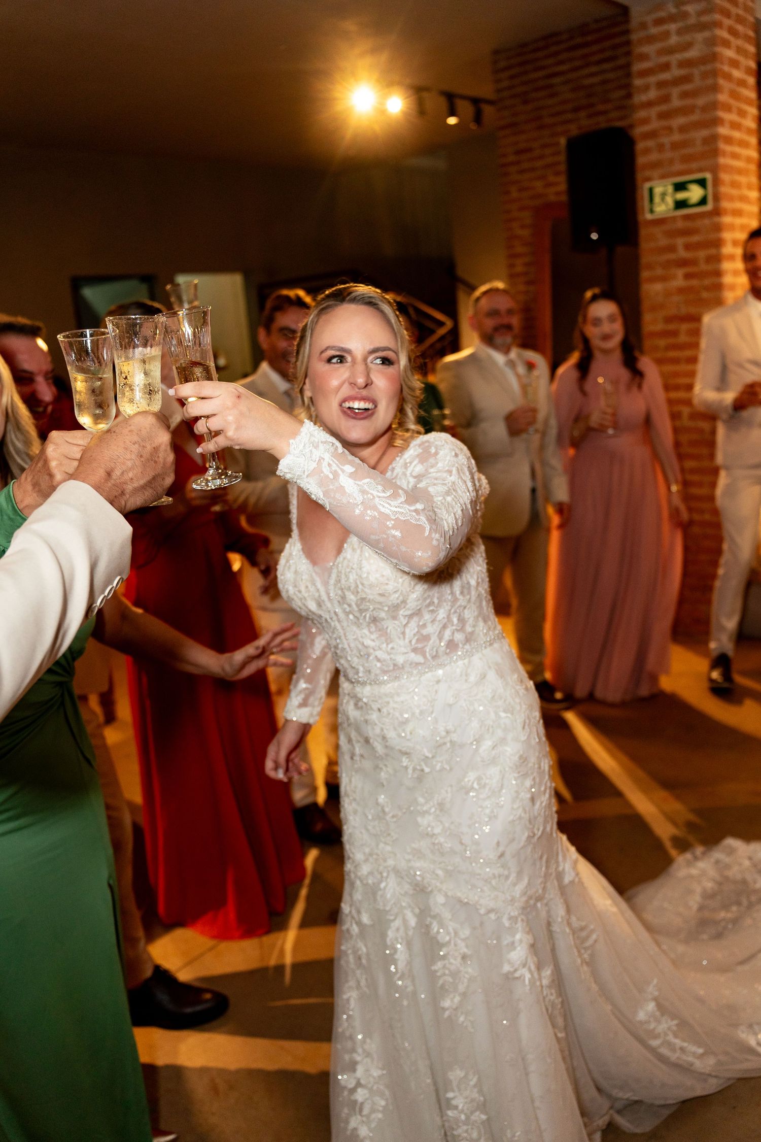 Bride in lace gown toasting champagne with guests at wedding reception celebration.