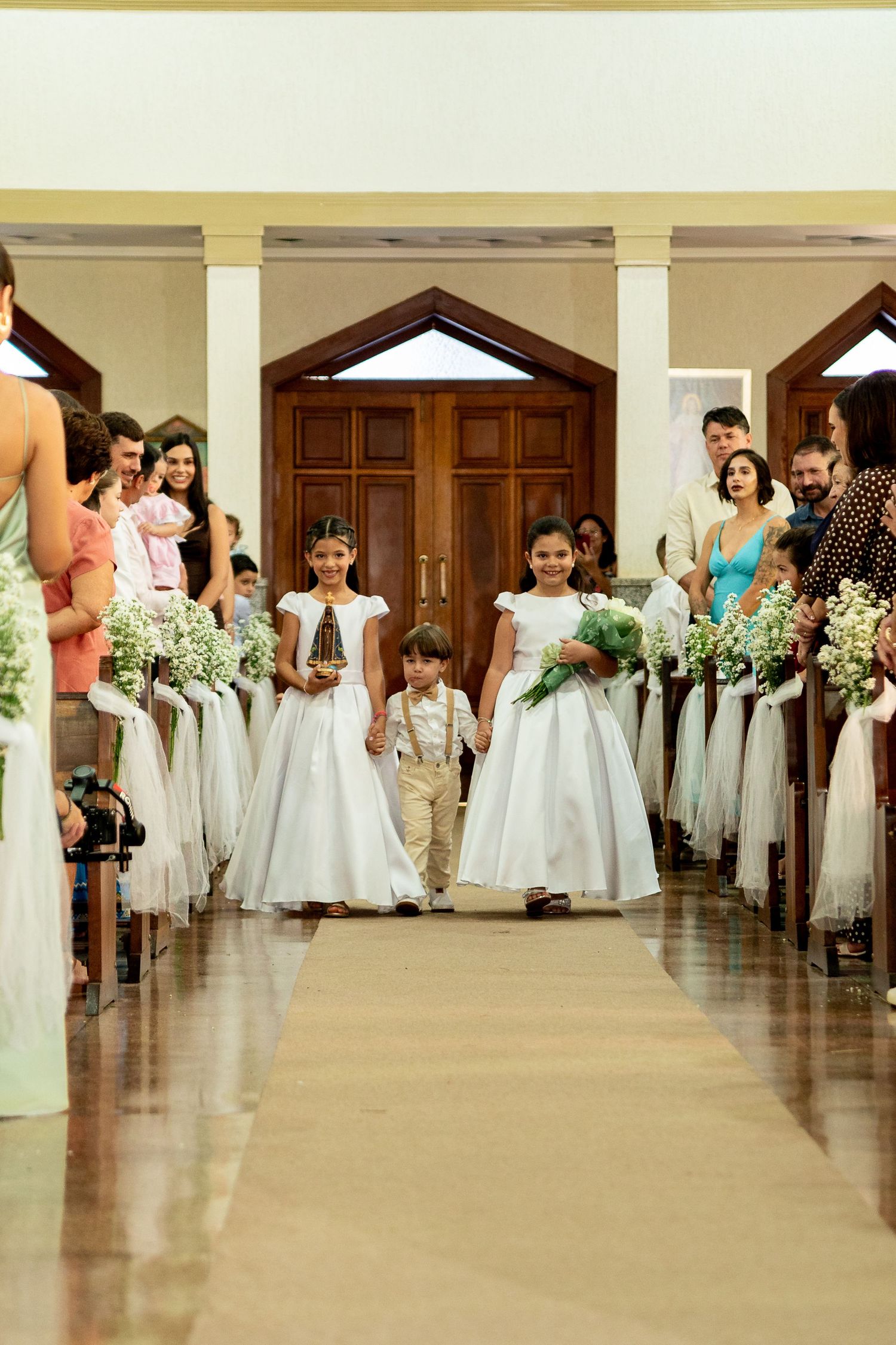 Flower girls and ring bearer walking down church aisle at wedding ceremony.