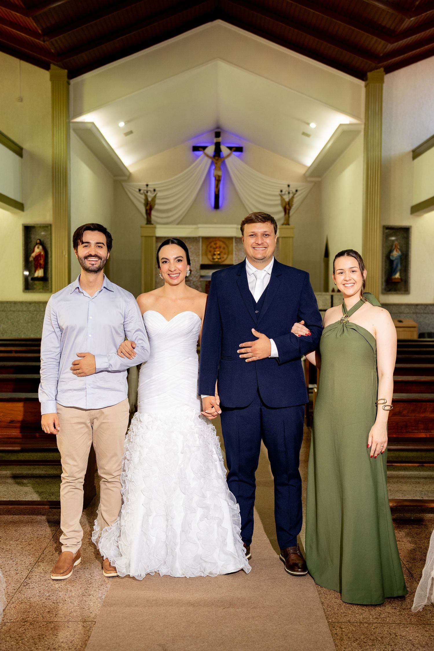 Wedding party of four smiling inside a church with cross and altar in background.