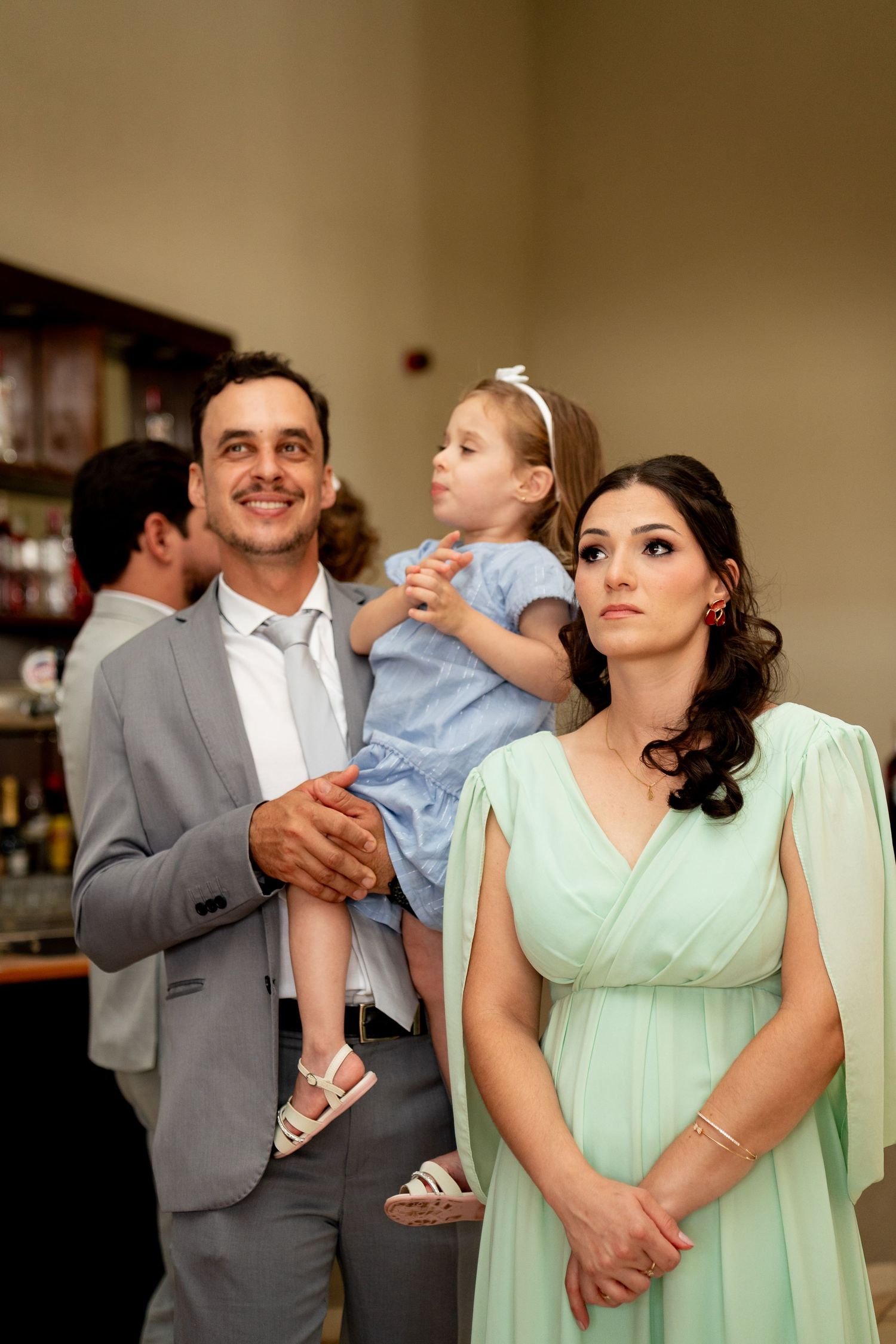 Family at formal event, man in gray suit holding young girl in blue dress beside woman in mint green gown.