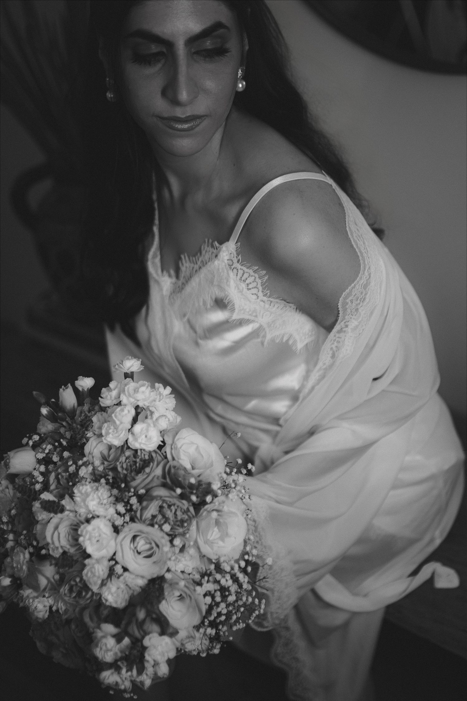 Black and white photo of a bride in a satin slip dress holding a lush bouquet of roses and wildflowers.