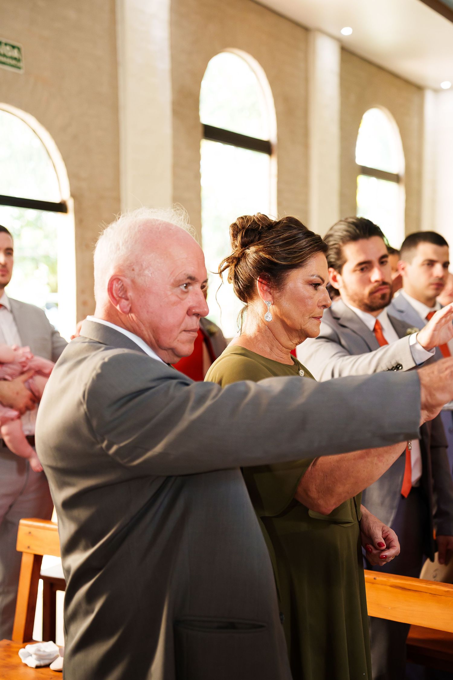 Elderly man and woman in formal attire taking a selfie during a wedding ceremony in a church.