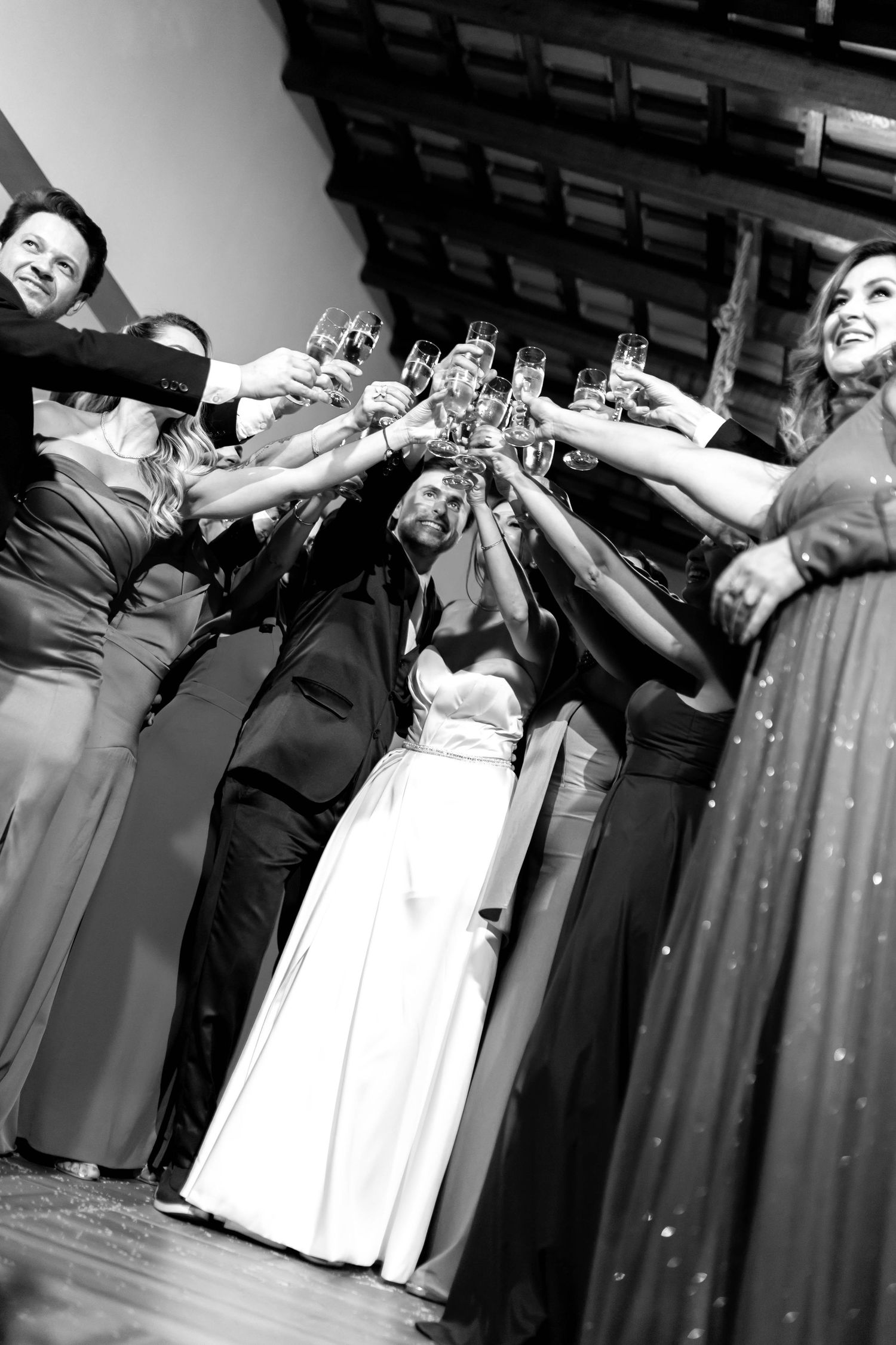 Black and white photo of a wedding party raising champagne glasses in a celebratory toast with bride and groom.