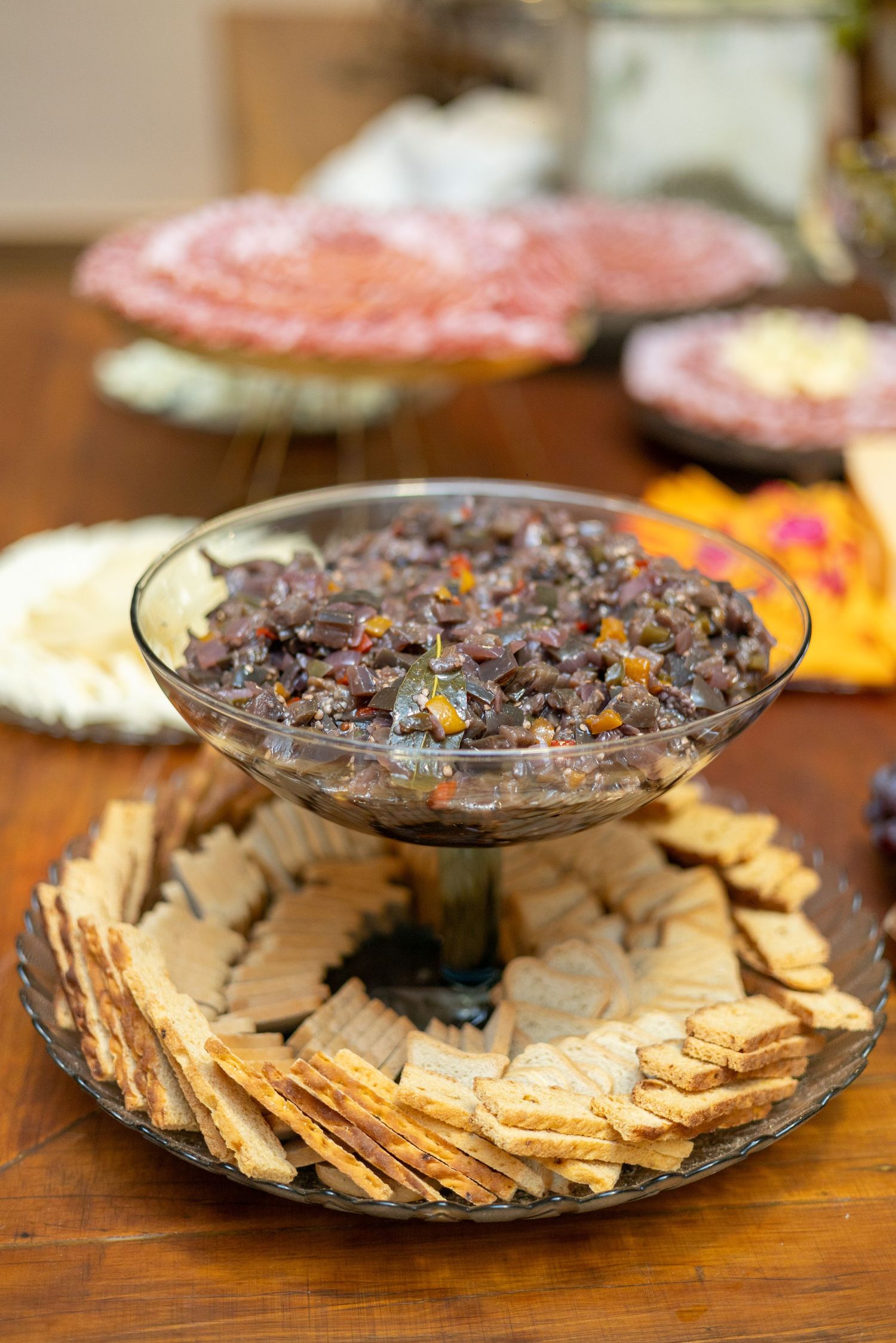 Glass bowl of black bean salsa served with crackers on a decorative platter at a party spread.
