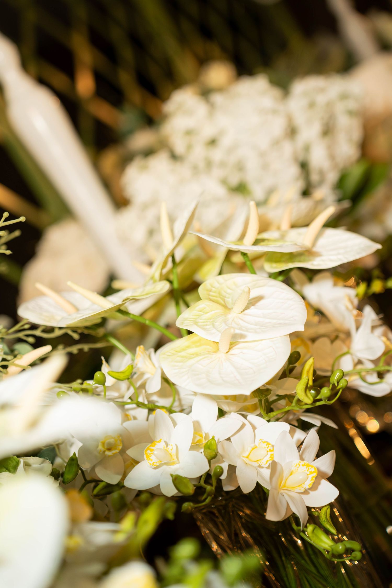 Elegant white anthurium and orchid floral arrangement with lush green foliage for wedding or event decor.