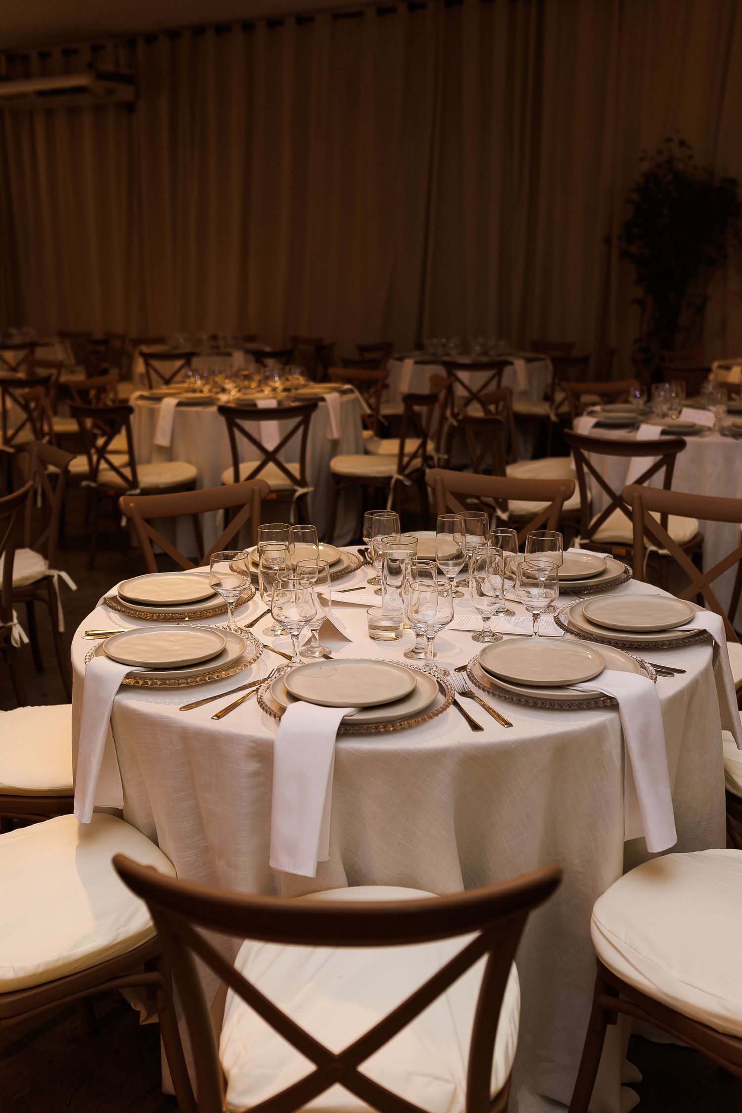 Elegant round banquet tables set with white linens, gold-rimmed plates, and crystal glasses in a warmly lit event hall.