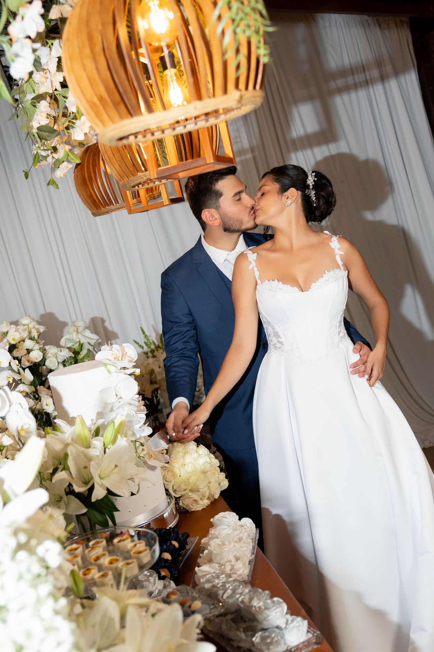 Bride and groom share a kiss at their wedding reception table adorned with white flowers and elegant decor.