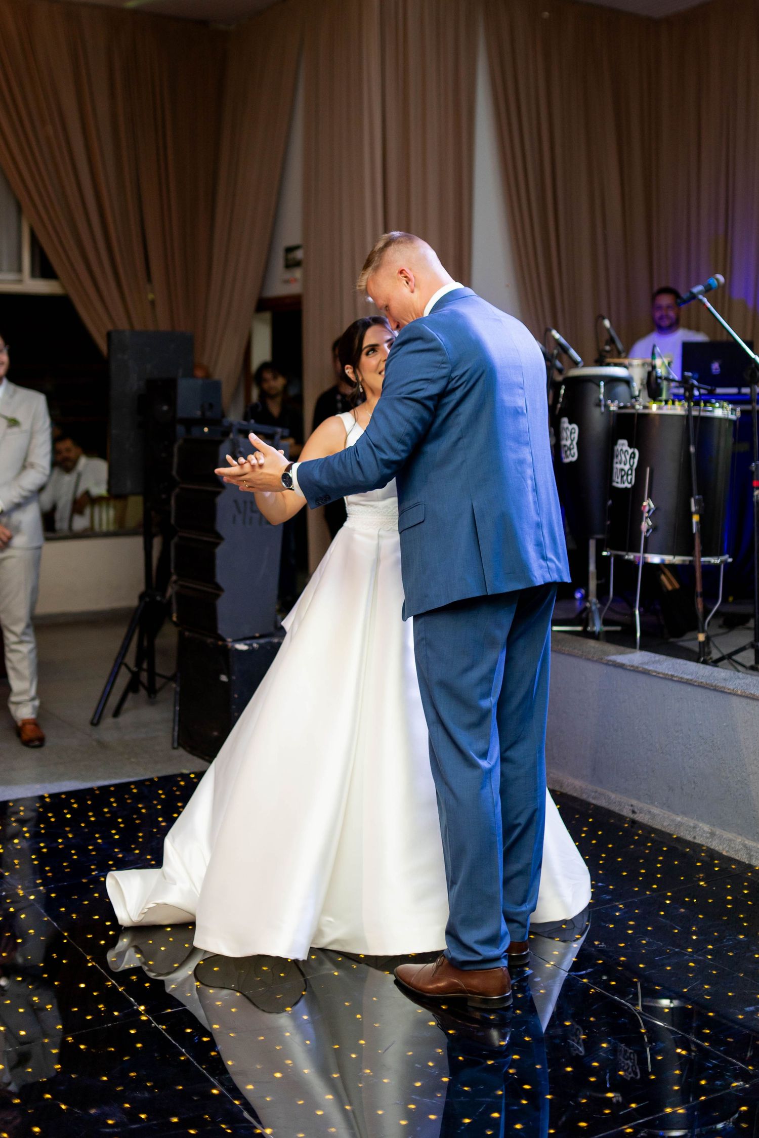 Bride and groom share their first dance on a dark dance floor at an elegant wedding reception venue.