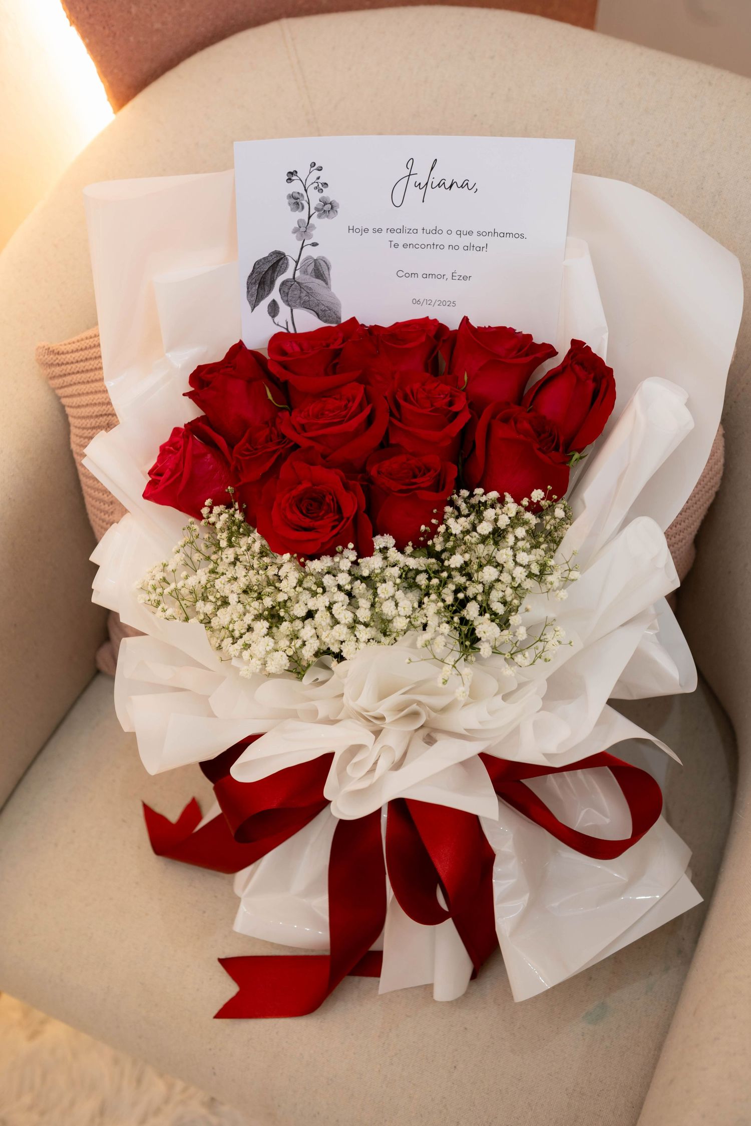 Elegant bridal bouquet of red roses and white baby's breath wrapped in white paper with a red ribbon and personalized card.