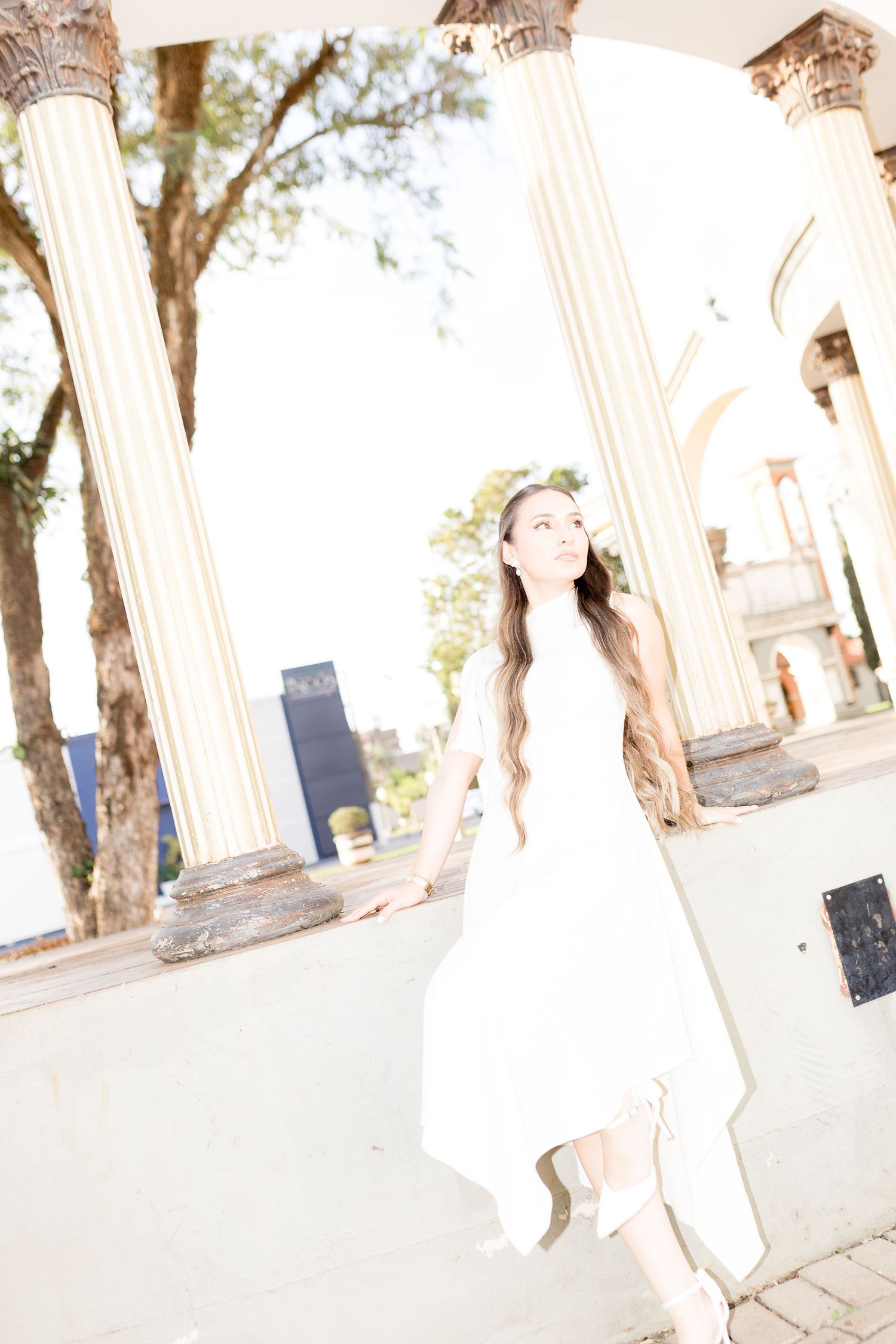 Young woman in white dress posing gracefully among classical columns in an outdoor architectural setting.