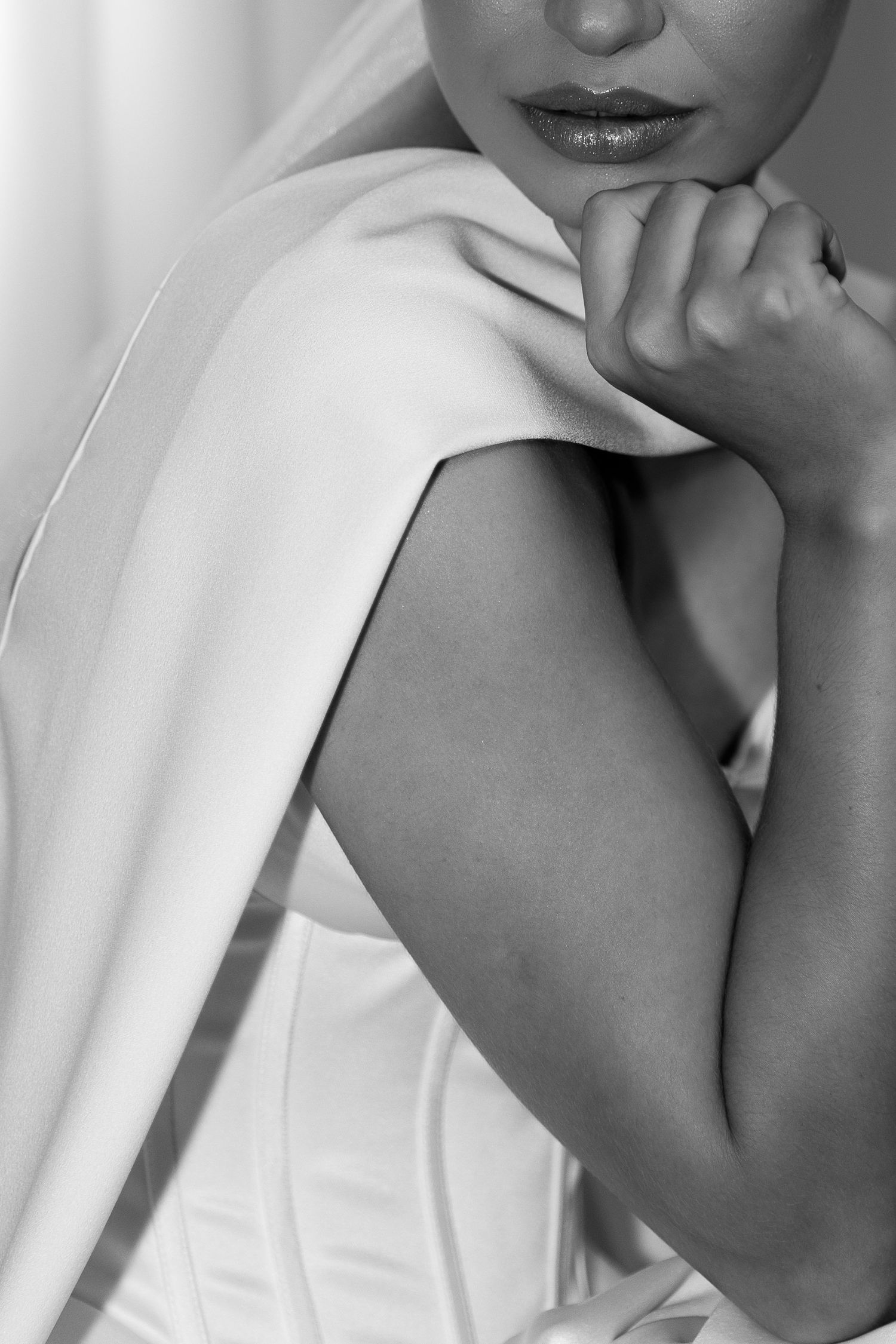 Black and white portrait of a bride in a white dress and veil, posing thoughtfully with her hand near her chin.