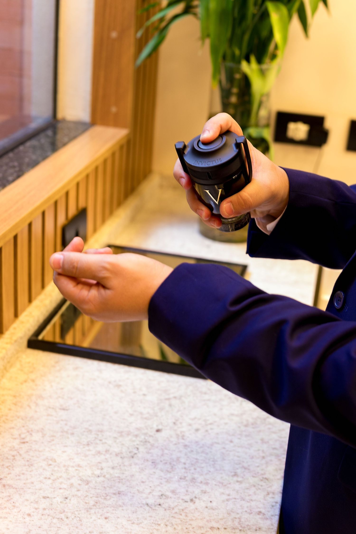 Hotel staff member in navy uniform applying hand sanitizer spray from a black dispenser bottle.