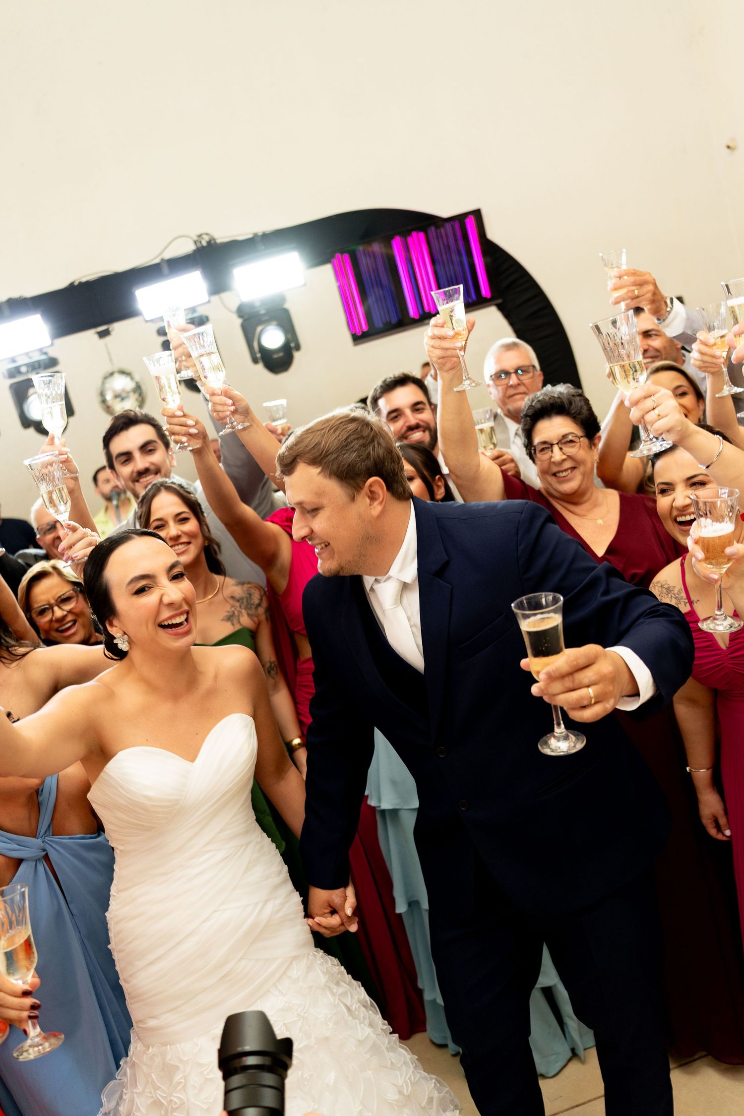 Bride and groom toast champagne with smiling wedding guests raising glasses in a joyful celebration.