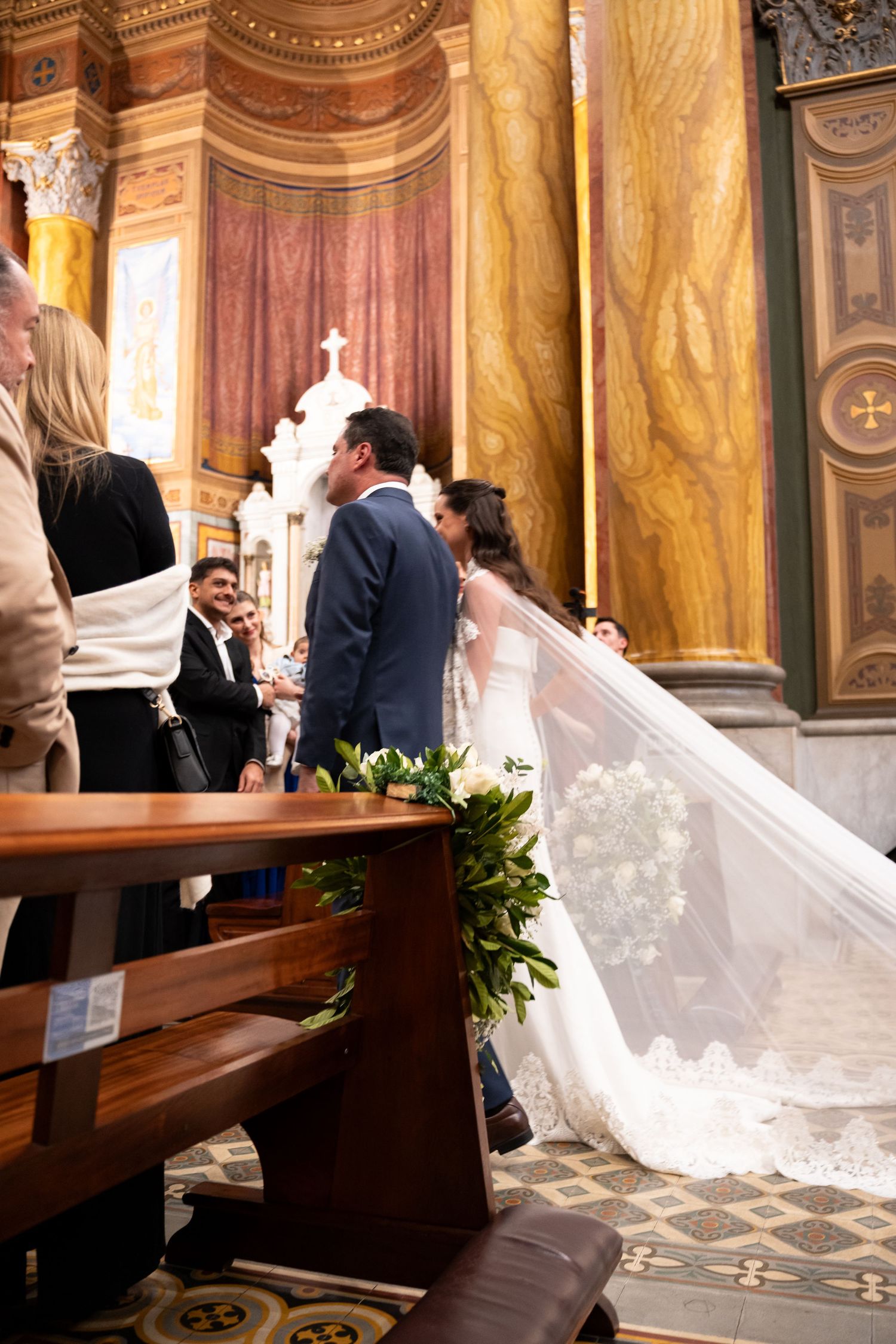 Bride in white gown with long veil at church altar during wedding ceremony with ornate marble decor.