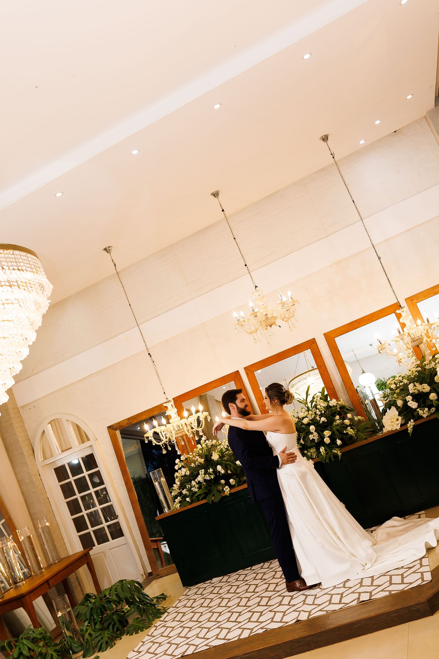 Bride and groom share their first dance in an elegant wedding venue adorned with chandeliers and floral arrangements.