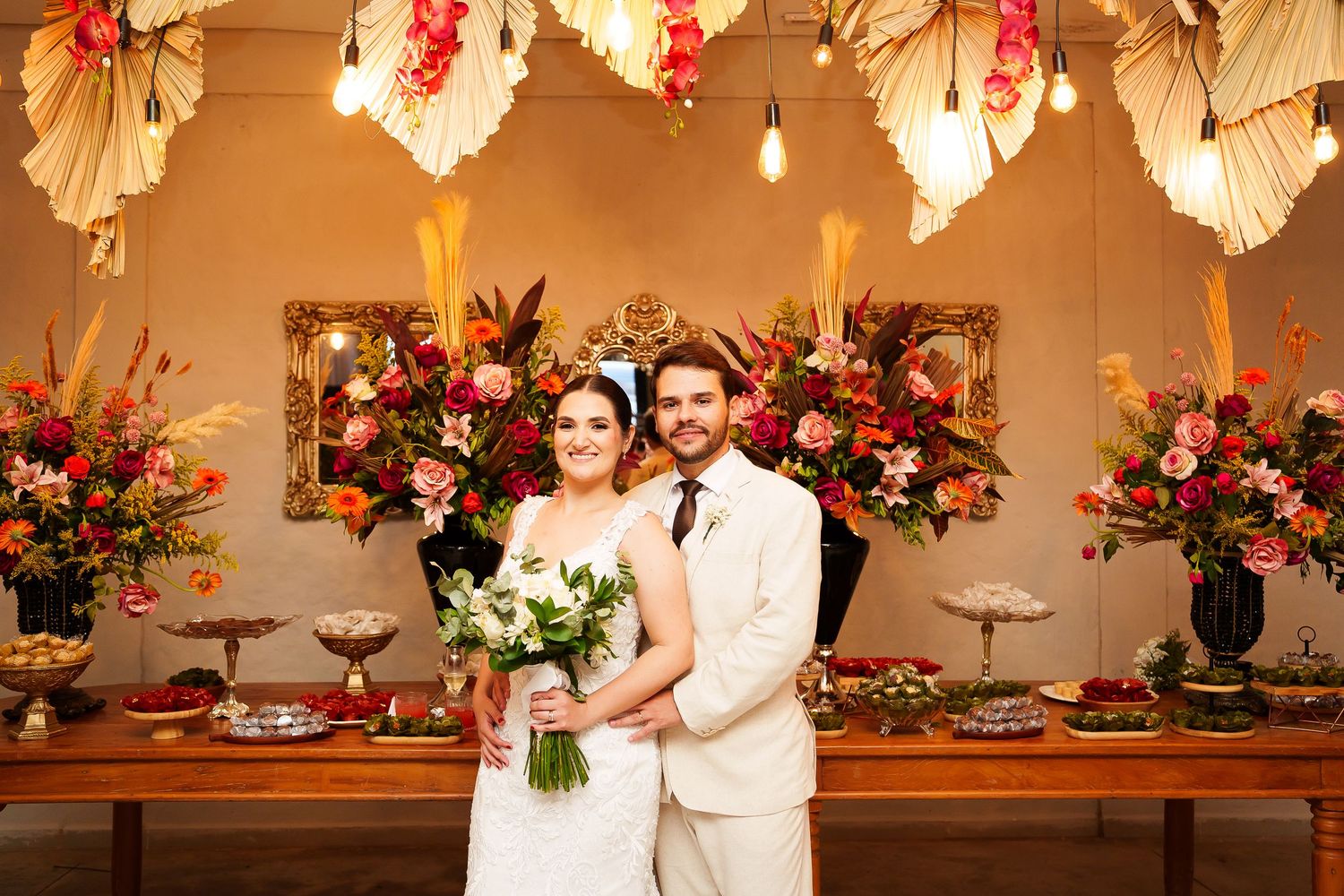 Bride and groom pose together at elegant wedding reception with vibrant floral arrangements and decorative paper fans.