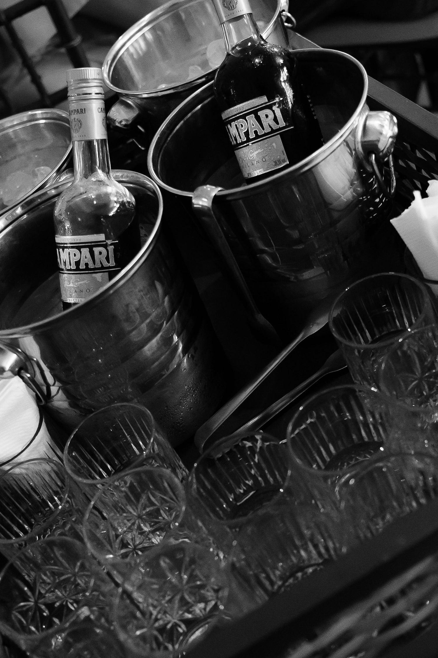 Black and white photo of Campari bottles in ice buckets with crystal glasses on a bar tray.