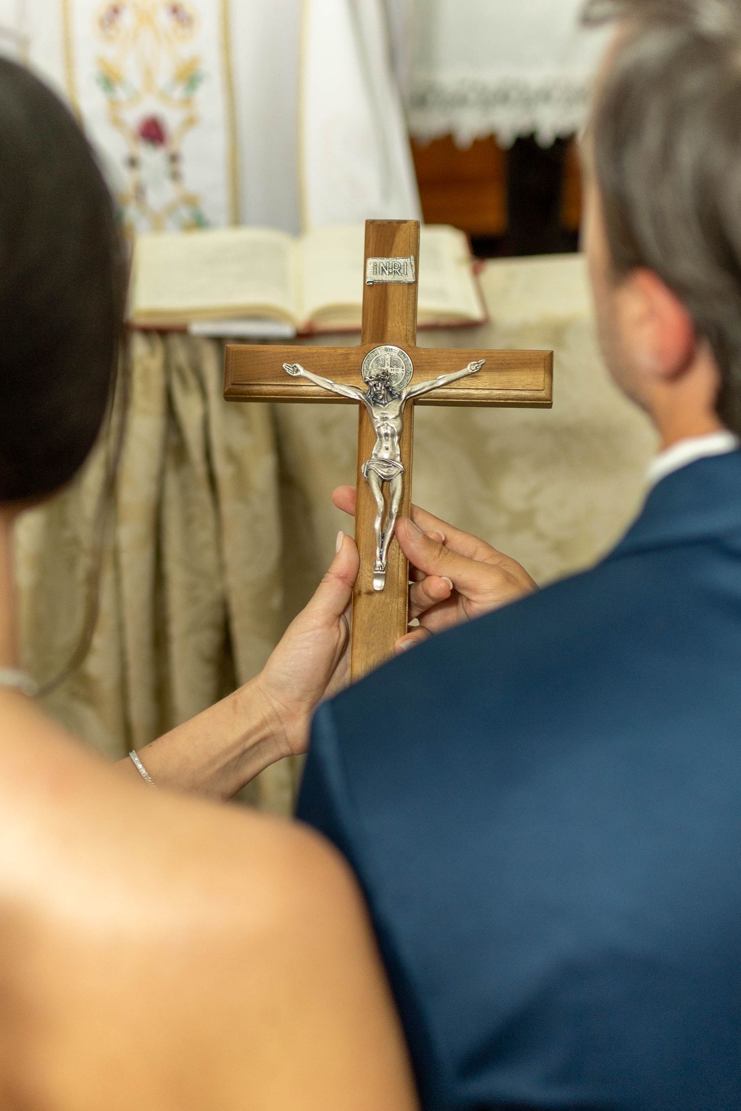 Couple holding a wooden crucifix with silver corpus during a Catholic wedding ceremony in church.