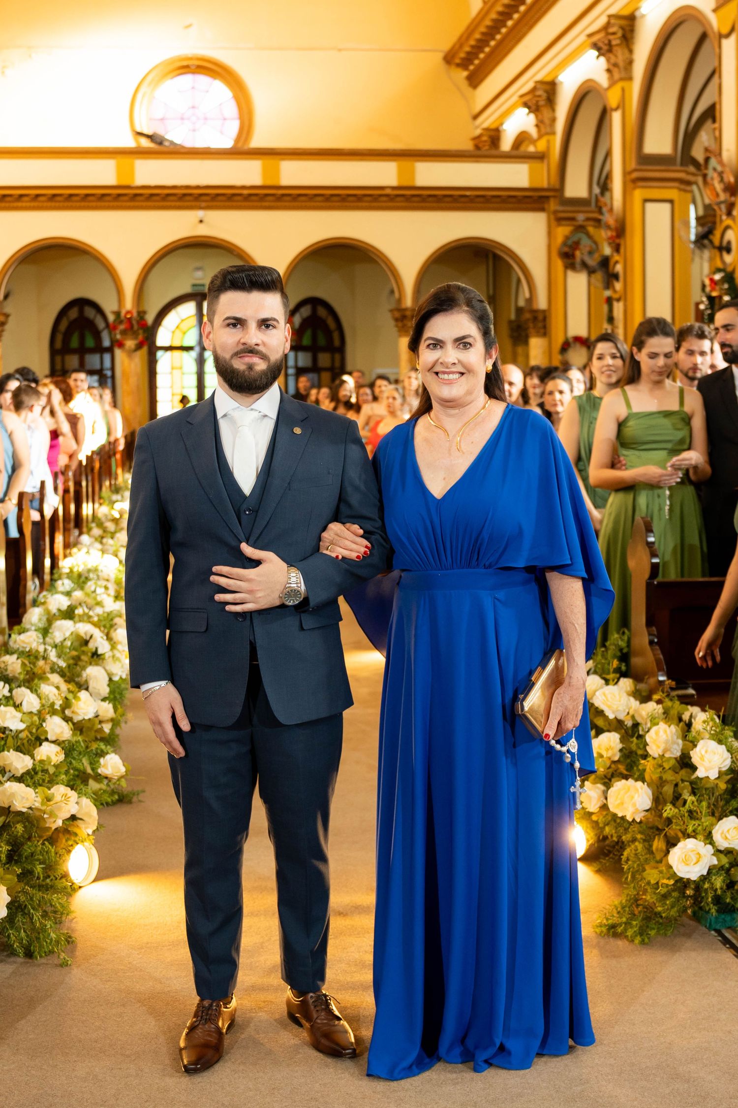 Couple posing in church aisle, man in navy suit, woman in royal blue gown, floral decorations, wedding ceremony.
