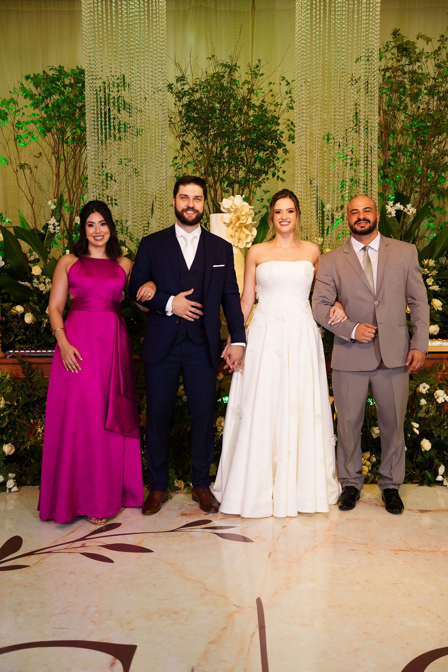 Wedding party of four posing elegantly, bride in white gown, groom in navy suit, guests in magenta dress and gray suit.