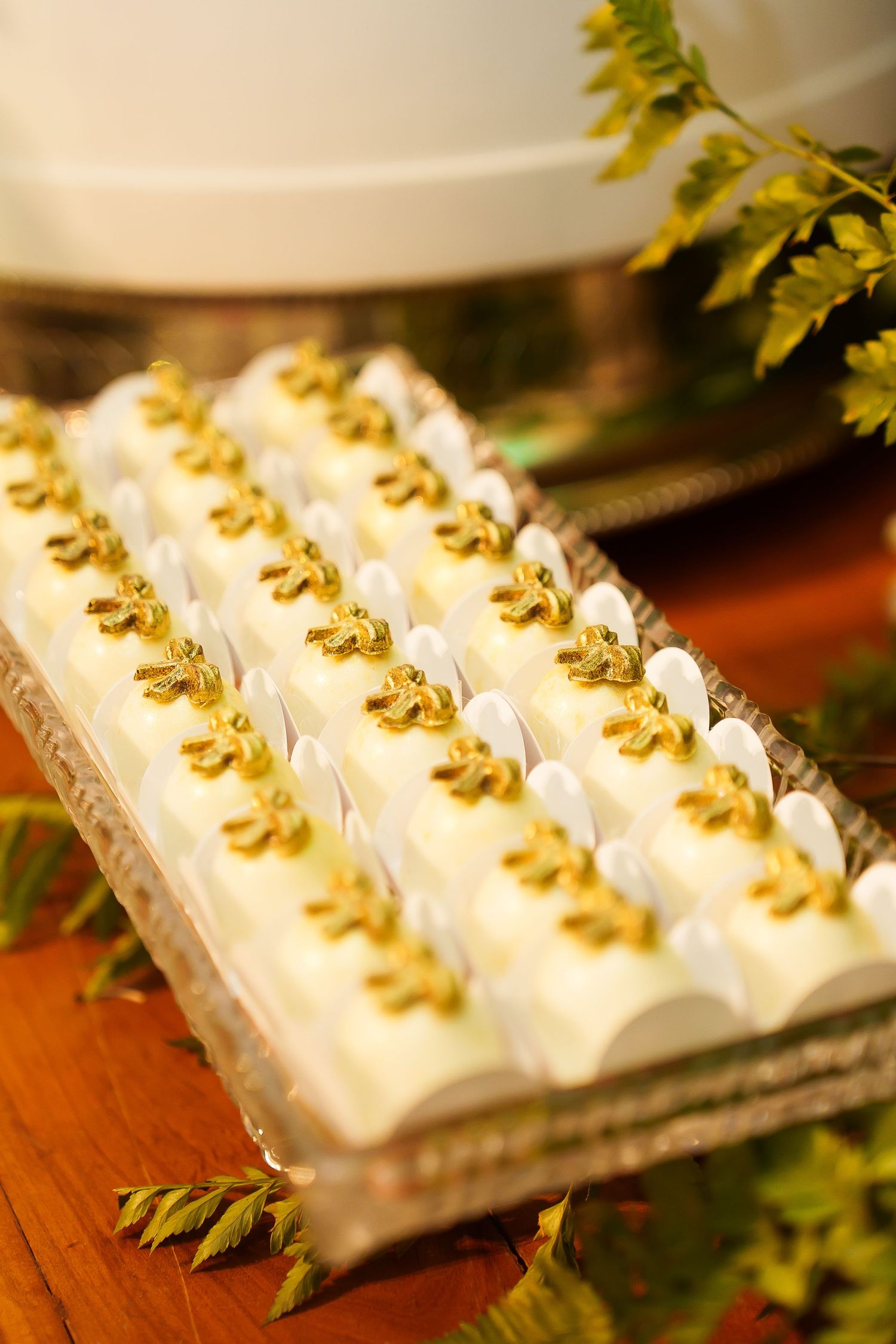 Elegant white petit fours with gold leaf decorations arranged on a silver tray at a wedding reception.