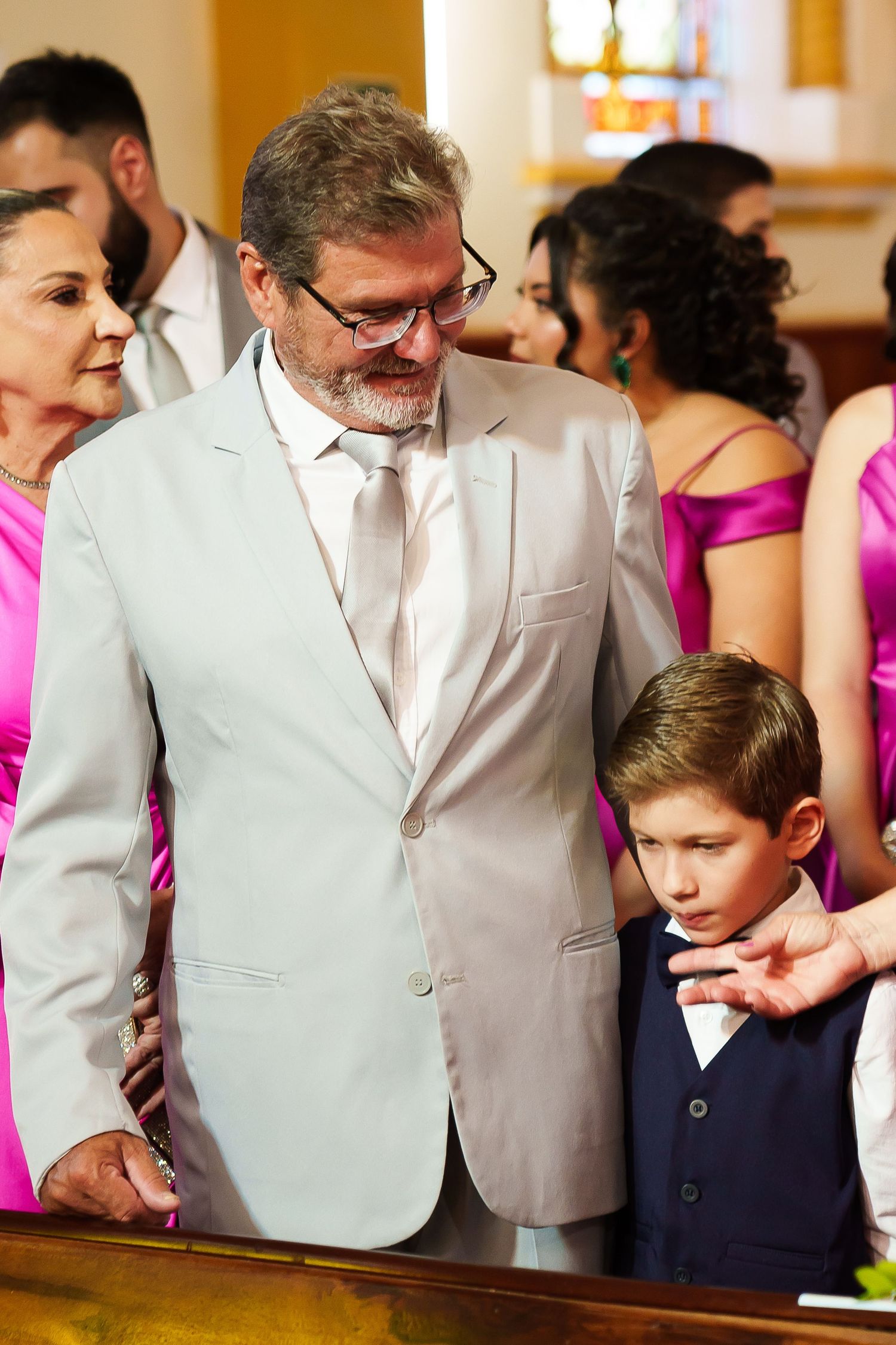 Man in light suit with boy in bow tie at a wedding ceremony inside a church.