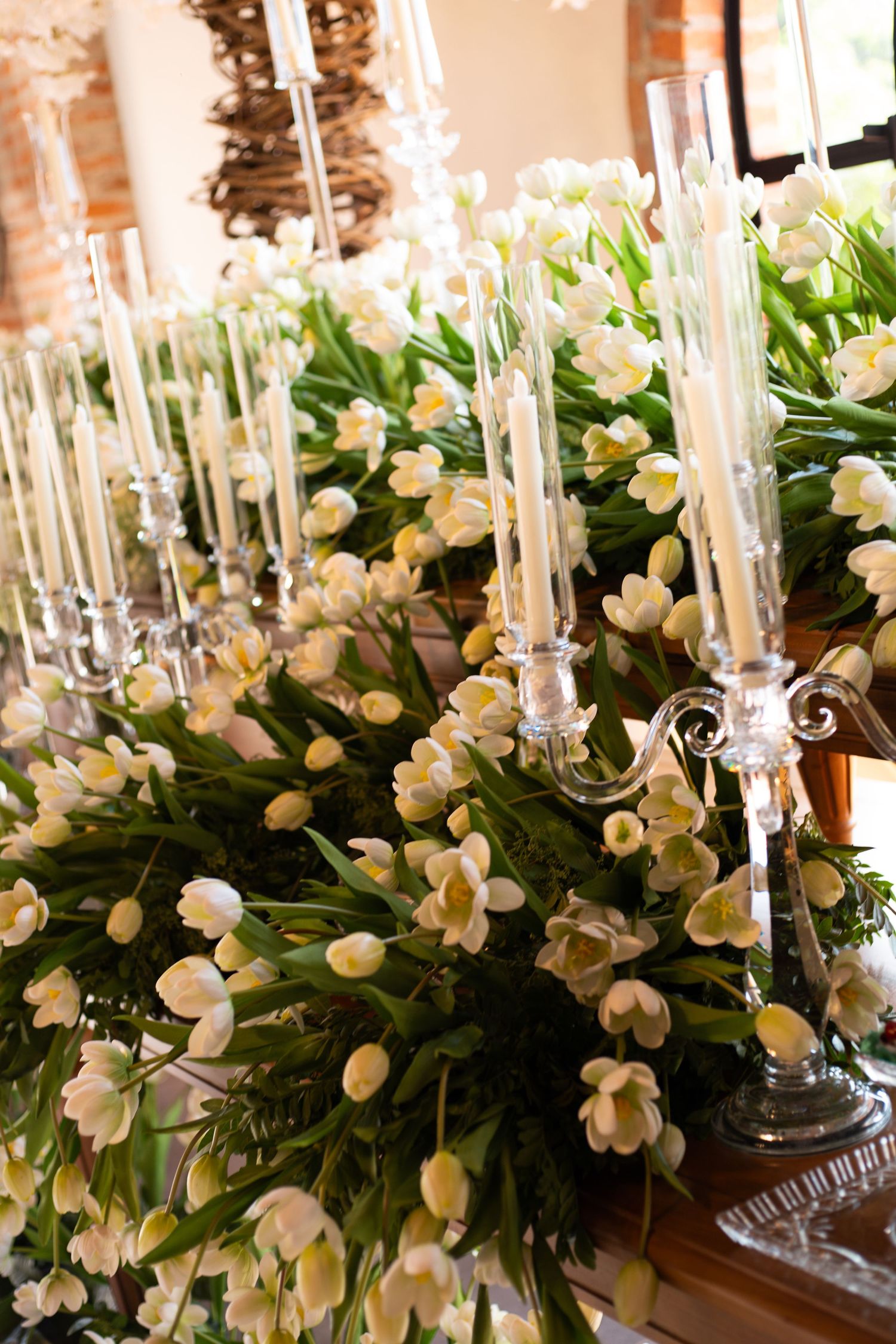 Elegant wedding centerpiece with white tulips and silver candelabras holding tall glass candles on a wooden table.