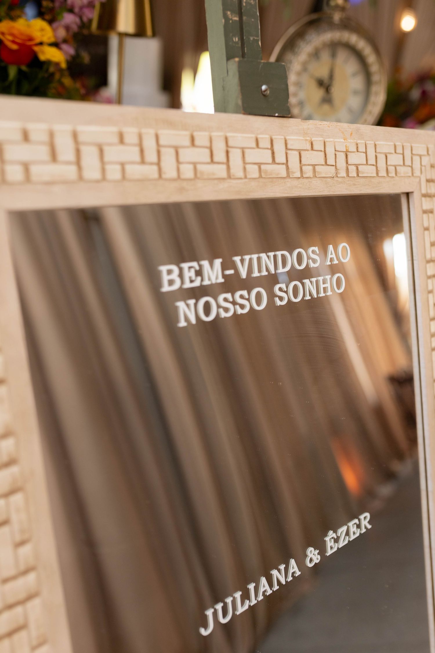 Elegant wedding welcome mirror sign reading Bem-Vindos ao Nosso Sonho for Juliana and Ezer displayed on wooden easel.