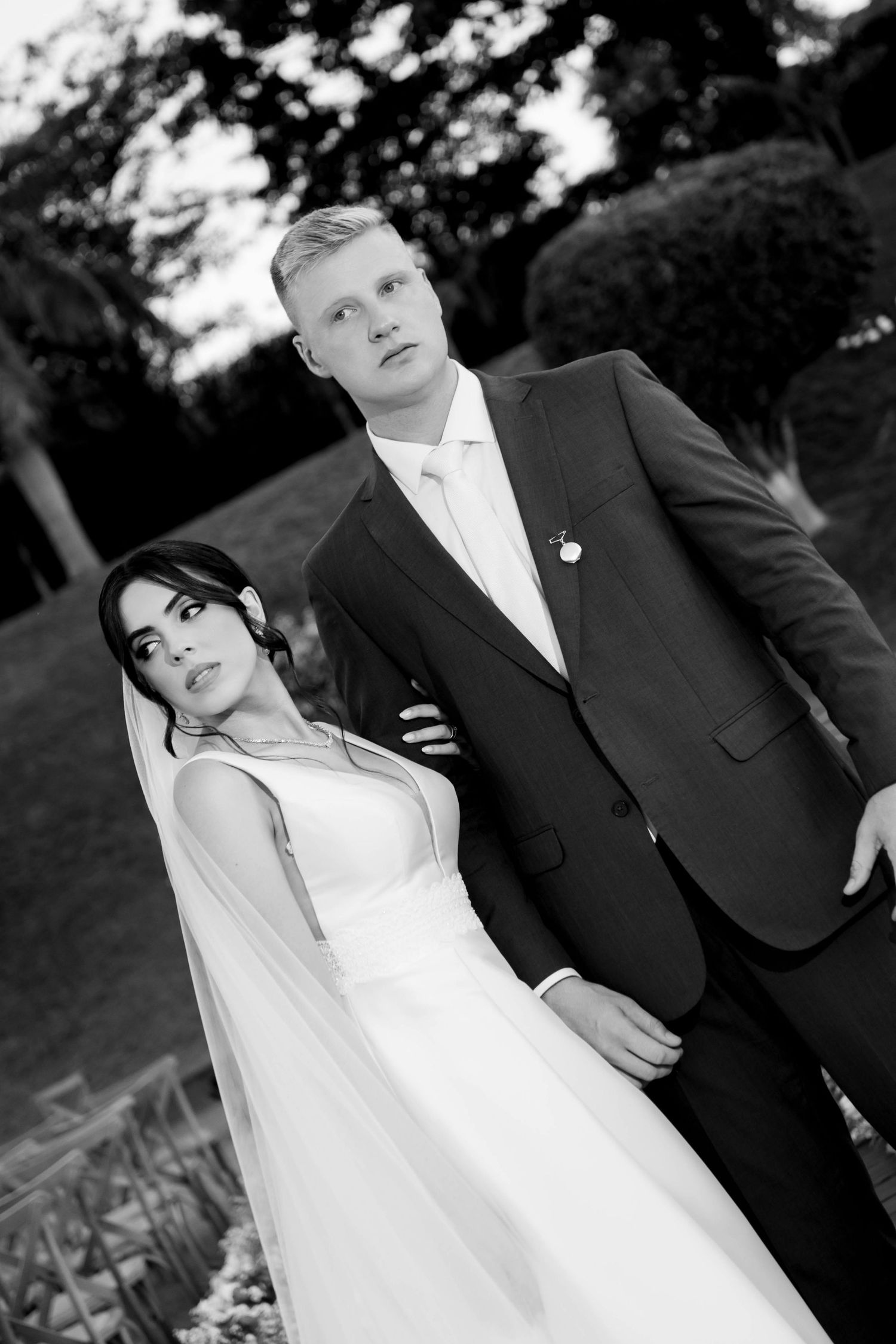 Black and white wedding photo of bride in white gown and groom in dark suit posing elegantly outdoors.