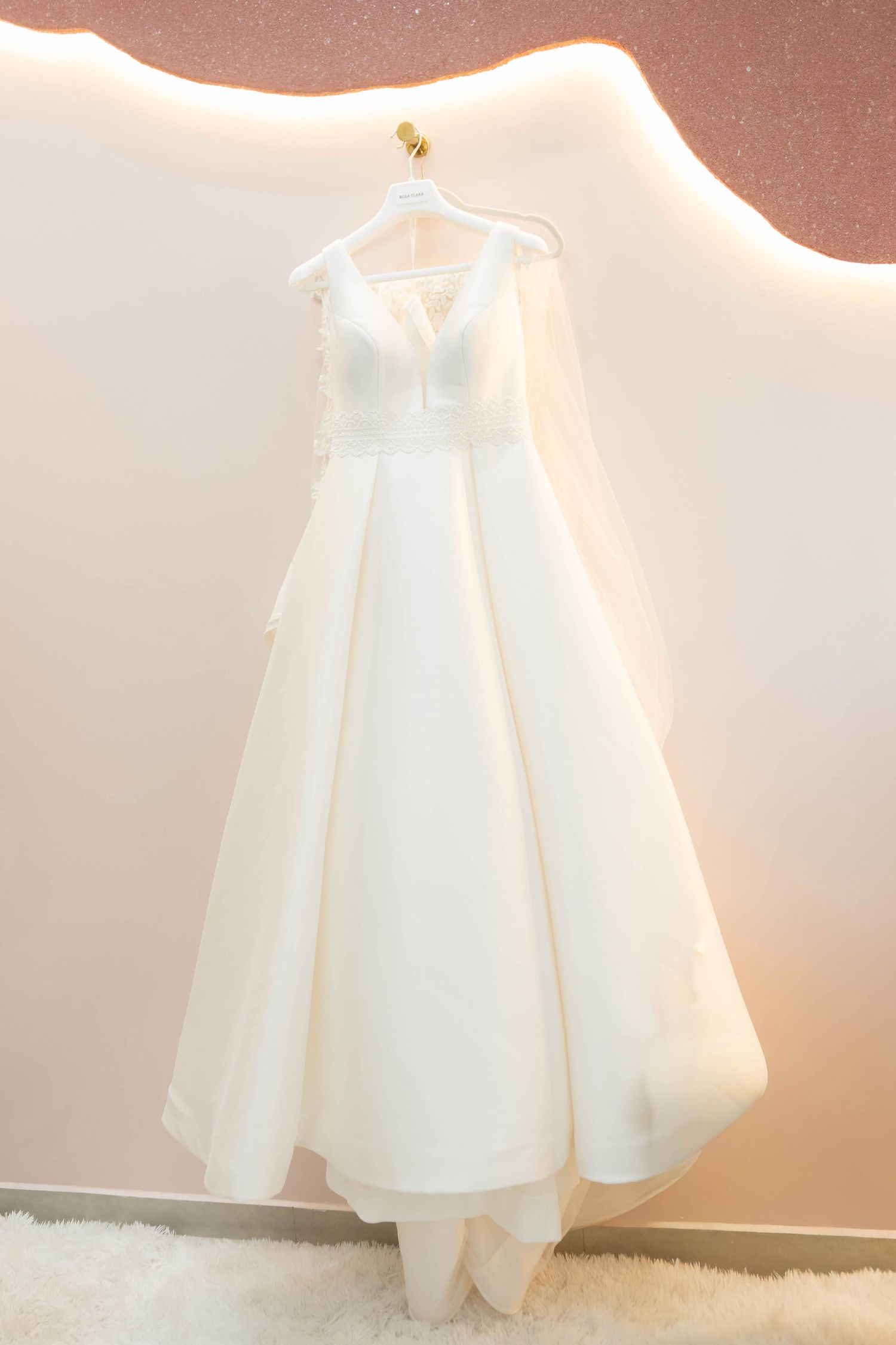 Elegant white A-line wedding dress with V-neckline and sheer veil hanging on display in a bridal boutique.