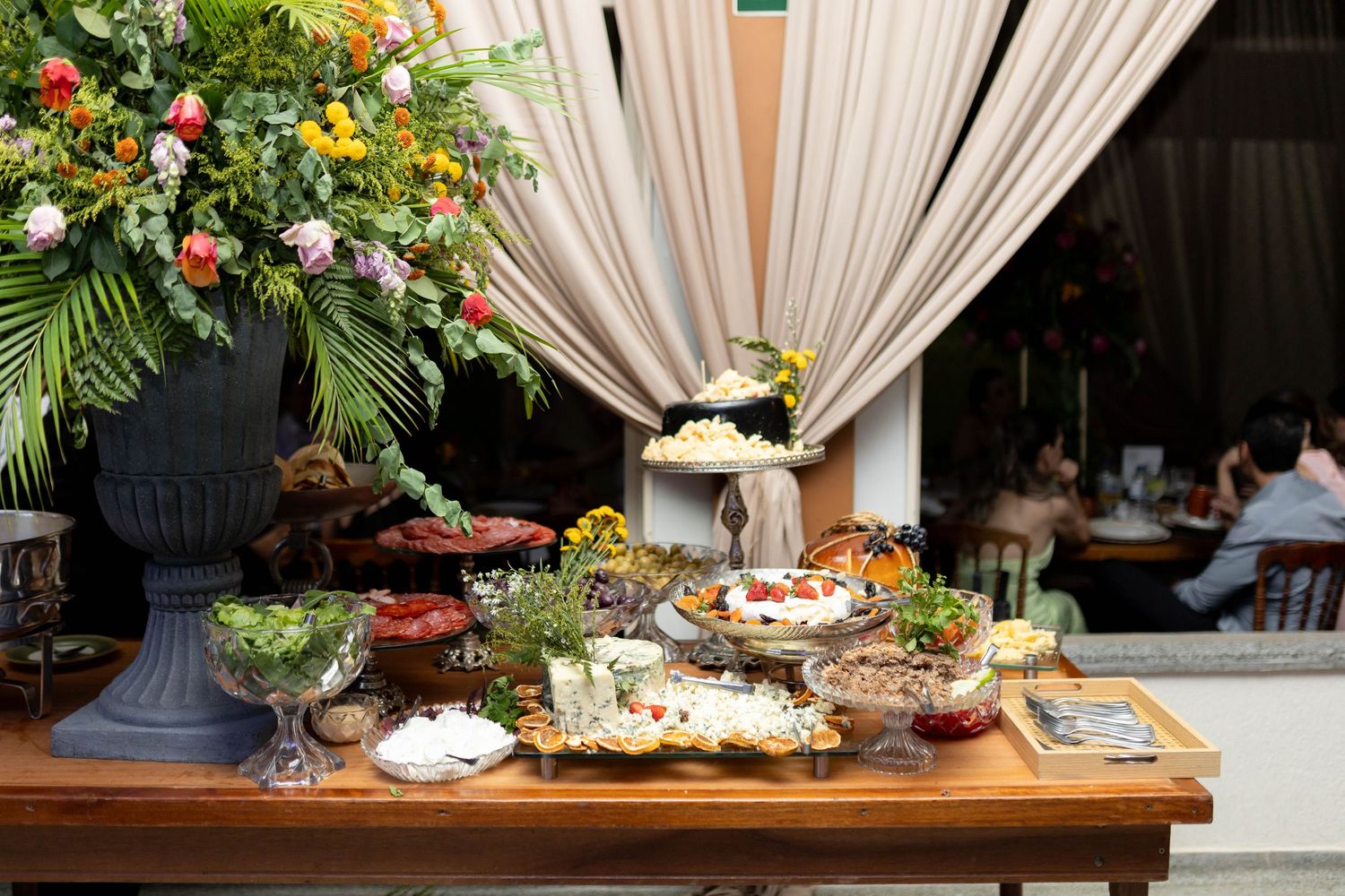 Elegant buffet table with floral arrangements, assorted dishes, and draped fabric backdrop for a formal event.