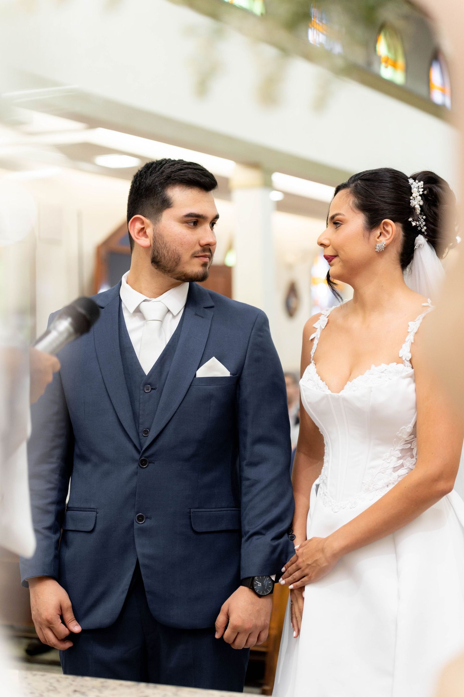 Bride and groom share a tender moment in a church, dressed in a white wedding gown and navy blue suit.
