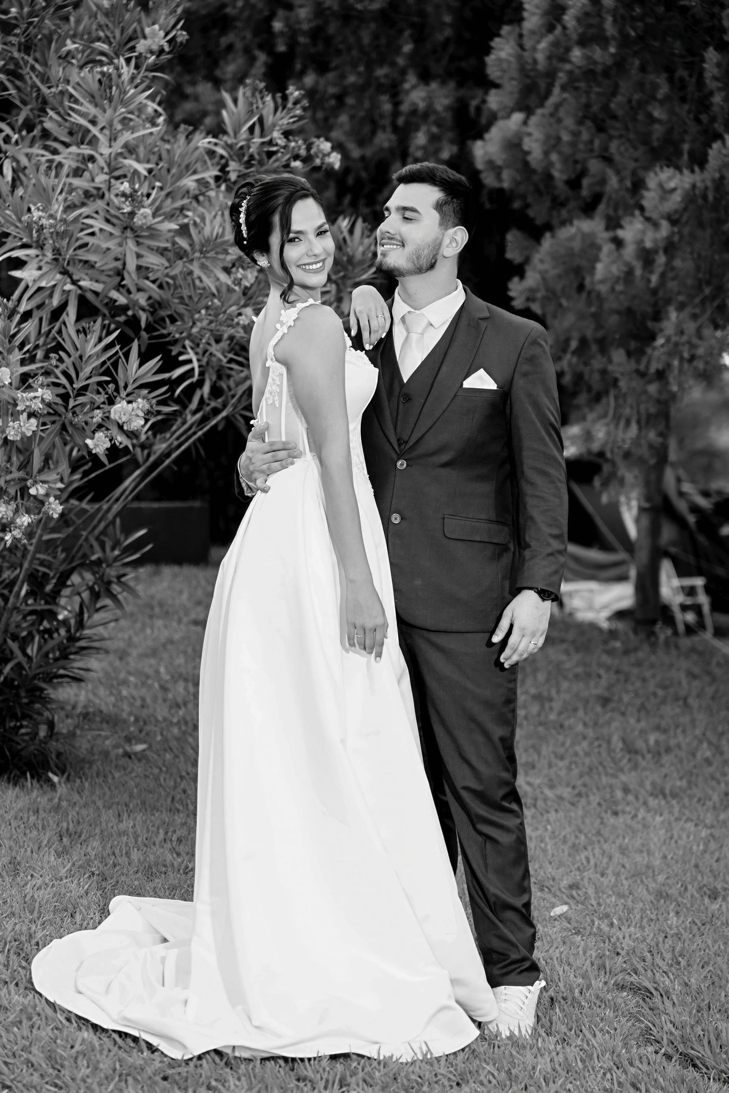 Black and white photo of a smiling bride in a white gown and groom in a dark suit posing together outdoors.