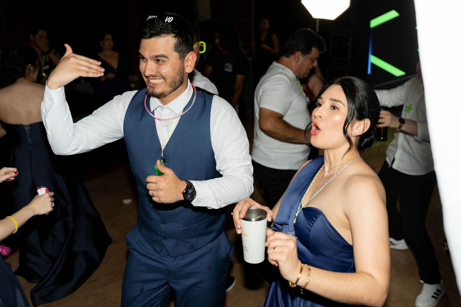A man in a navy vest and woman in a blue dress dance and smile at a formal party event.