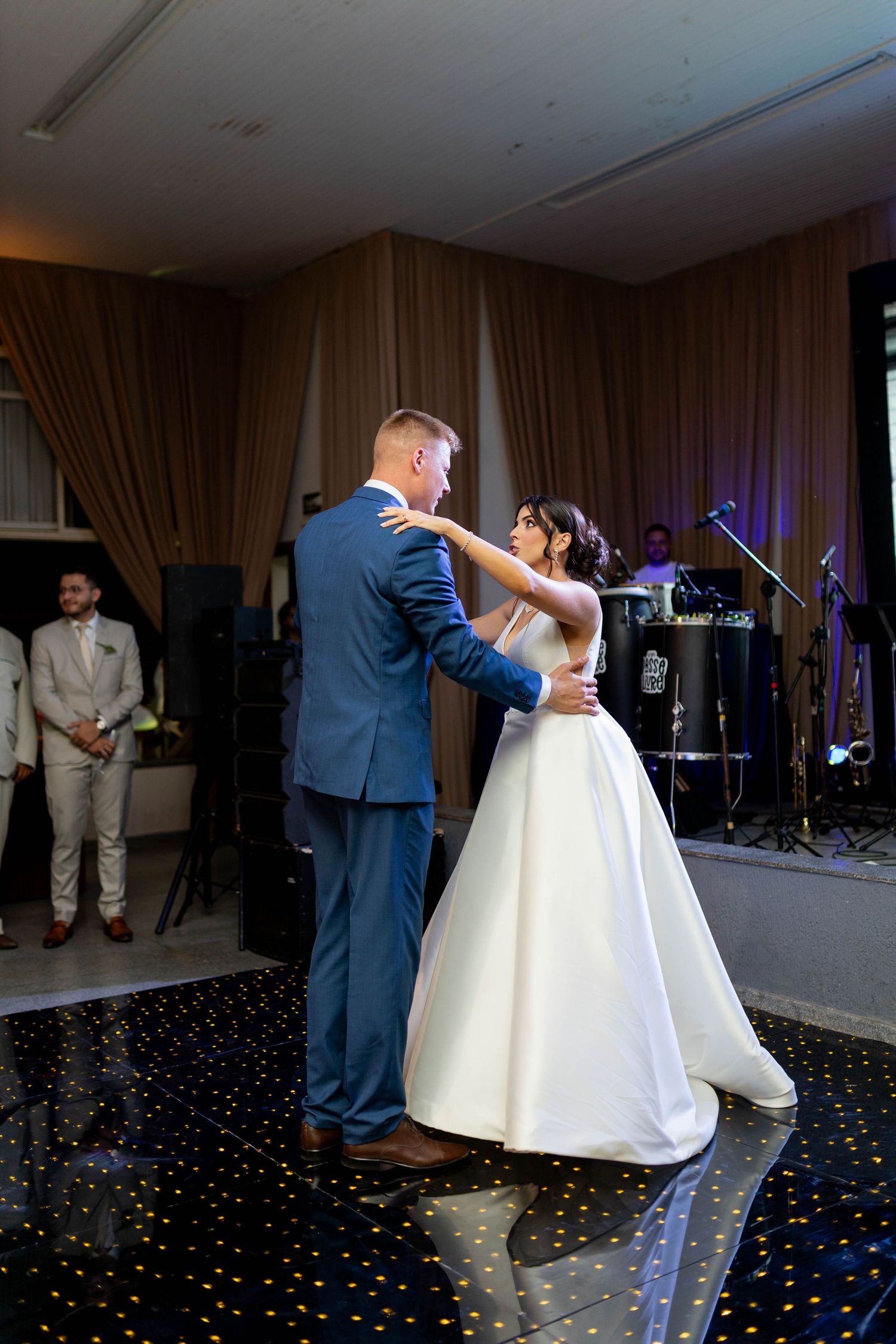 Bride and groom share their first dance on a black dance floor at an elegant wedding reception with a live band.