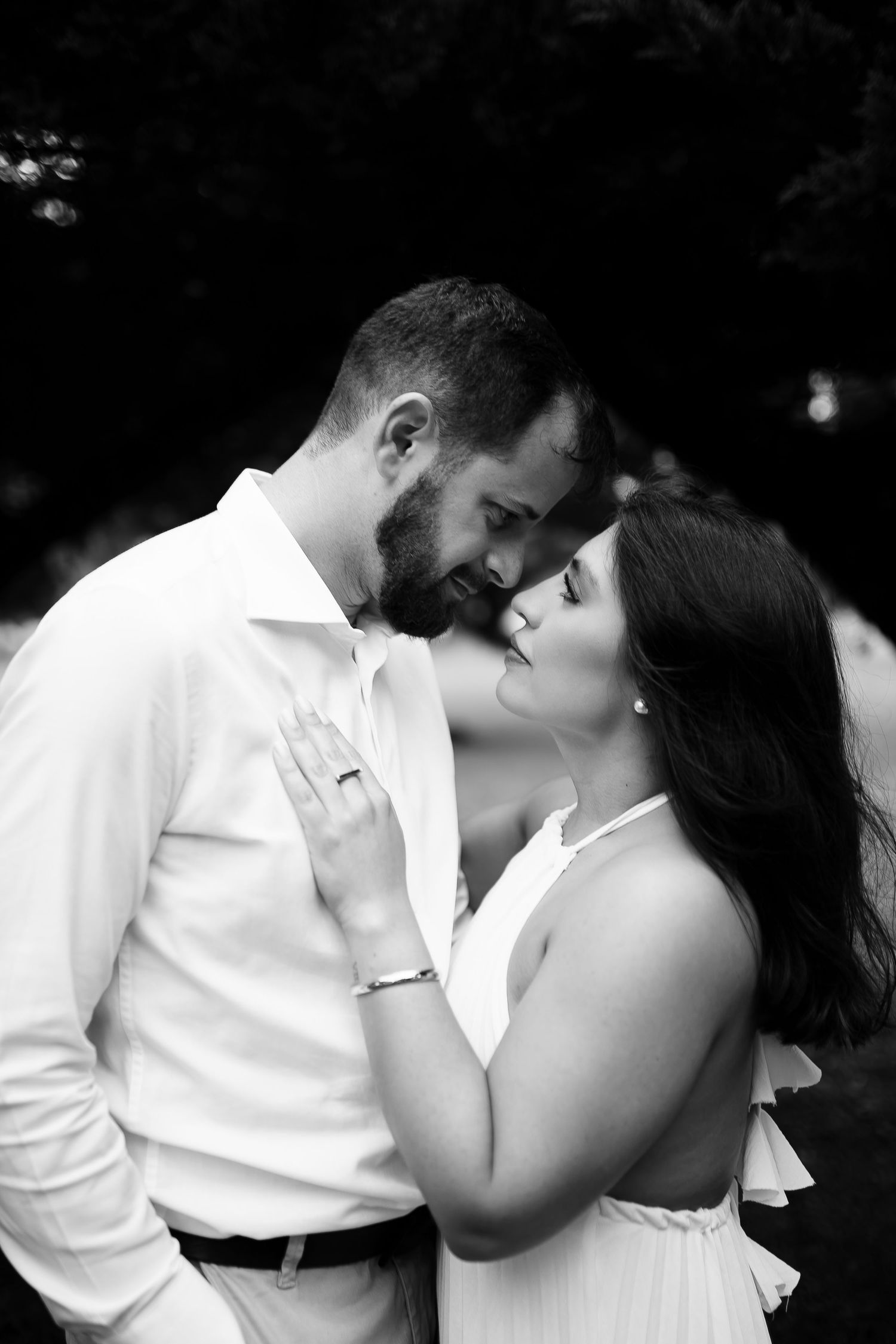 Black and white photo of a romantic couple in white attire sharing an intimate moment outdoors.