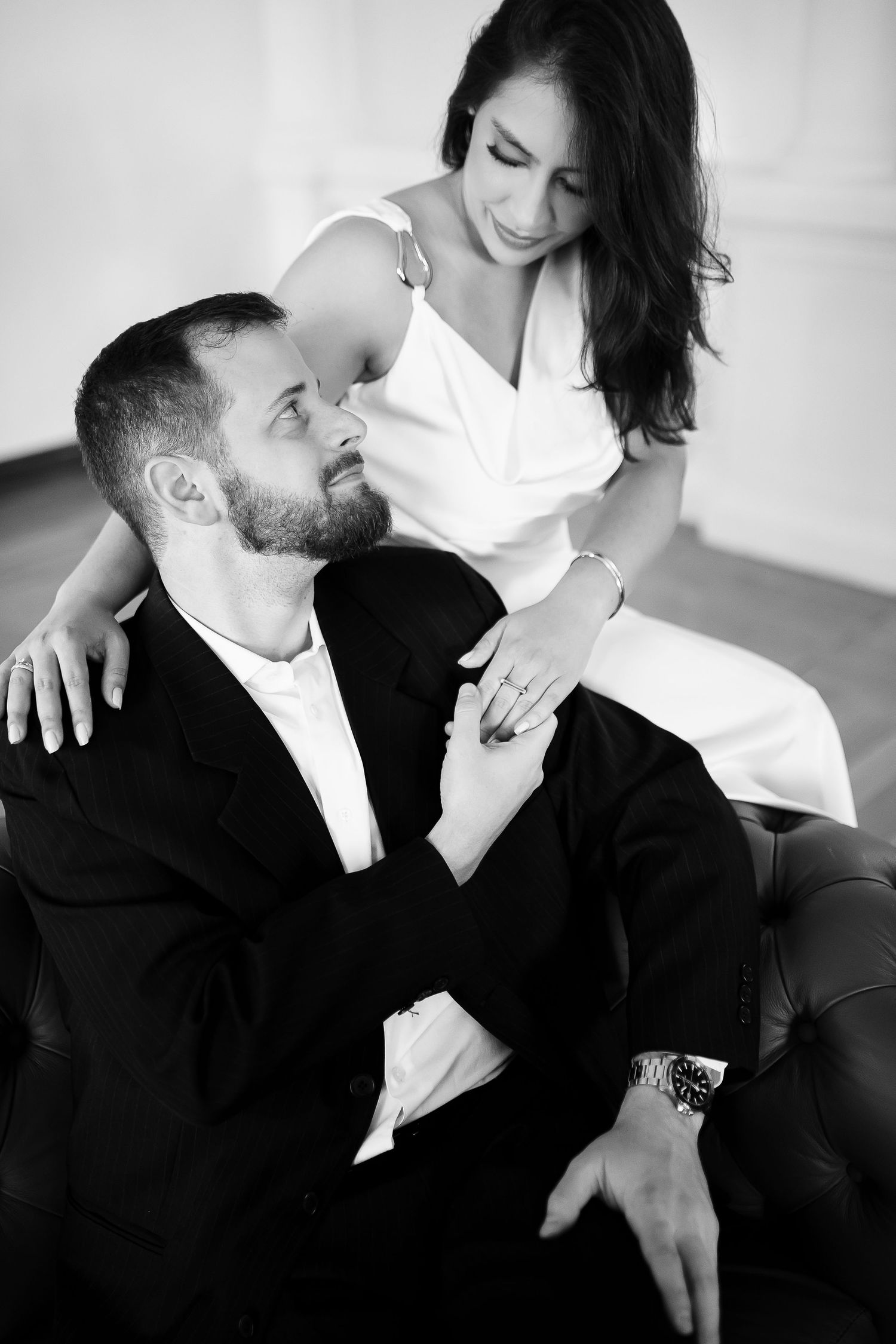 Black and white photo of a bearded man in suit and woman in white dress sharing a romantic moment.