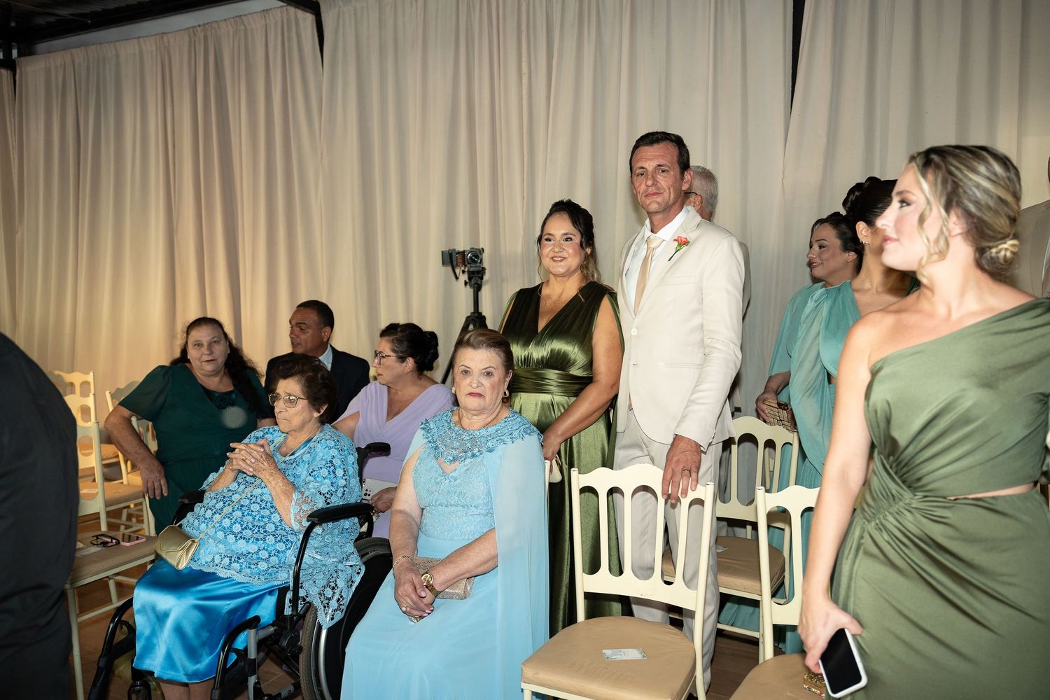 Elegant wedding reception with guests in formal attire, including a woman in wheelchair, posing together indoors.