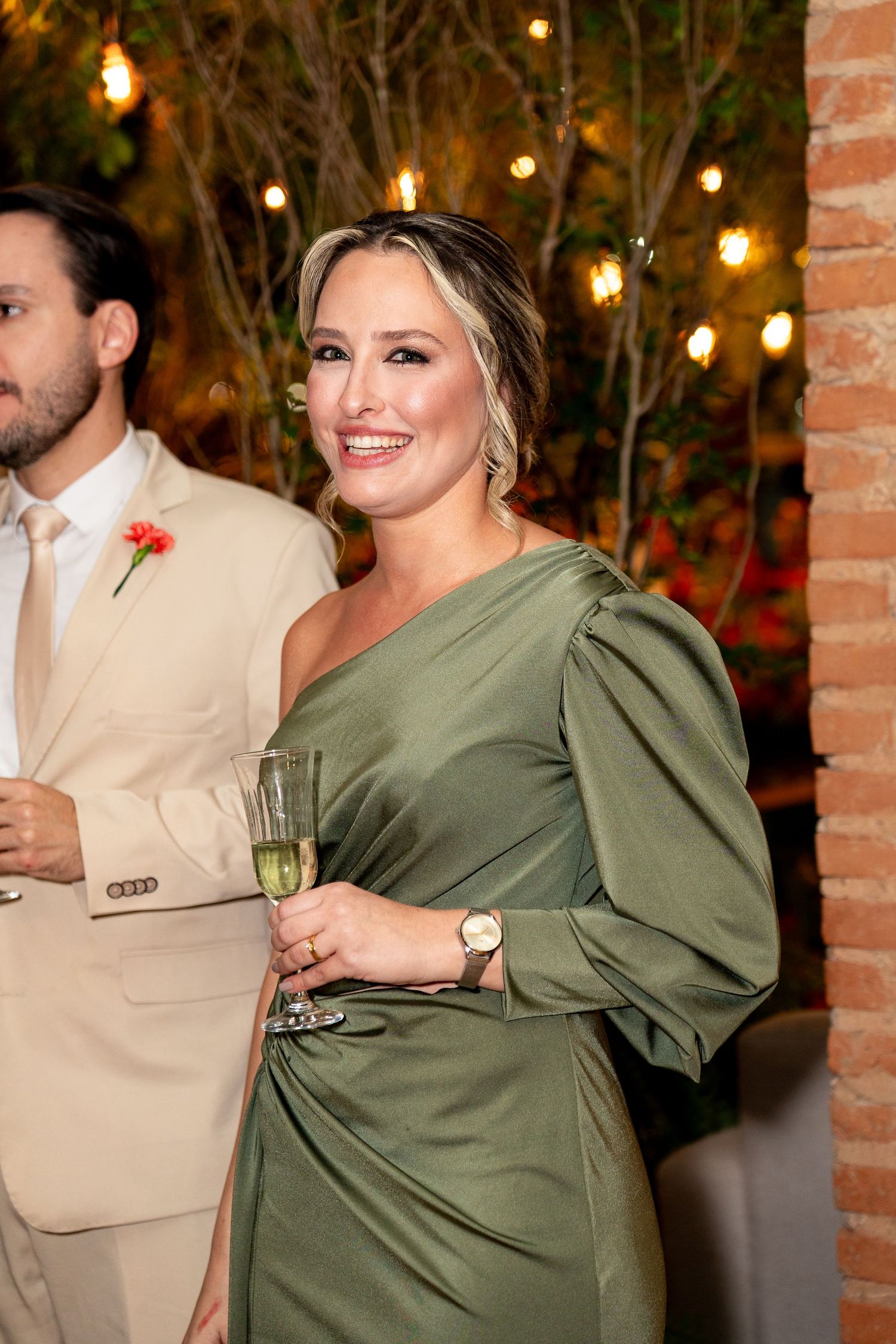 Woman in elegant green satin one-shoulder dress holding champagne glass at a formal evening event.