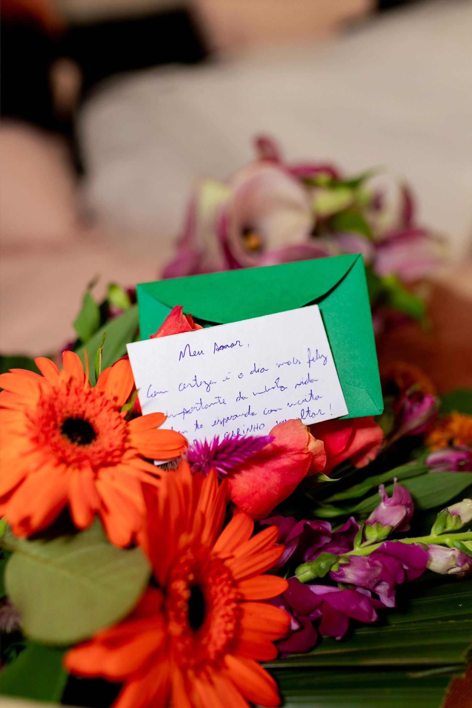 Colorful bouquet of orange gerbera daisies and purple flowers with a handwritten note card and green envelope.