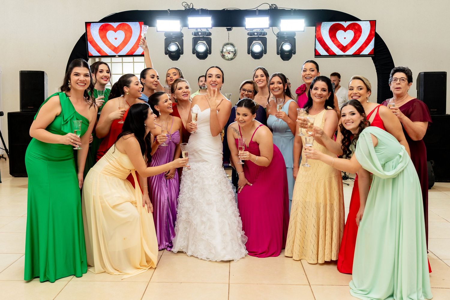 Bride poses with colorful bridesmaids in elegant gowns at a decorated wedding reception venue.