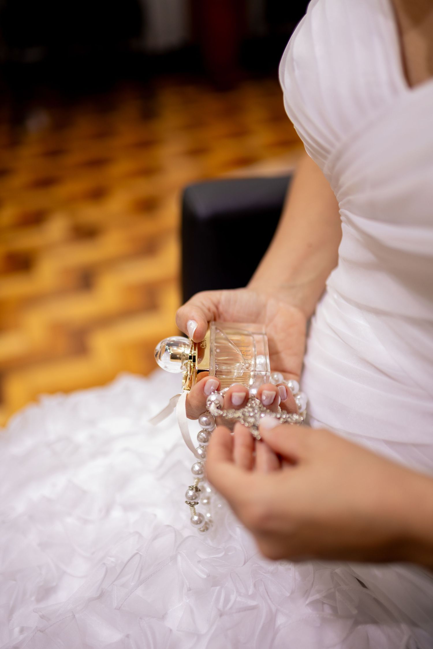 Bride in white dress holding a perfume bottle and pearl necklace on her wedding day.